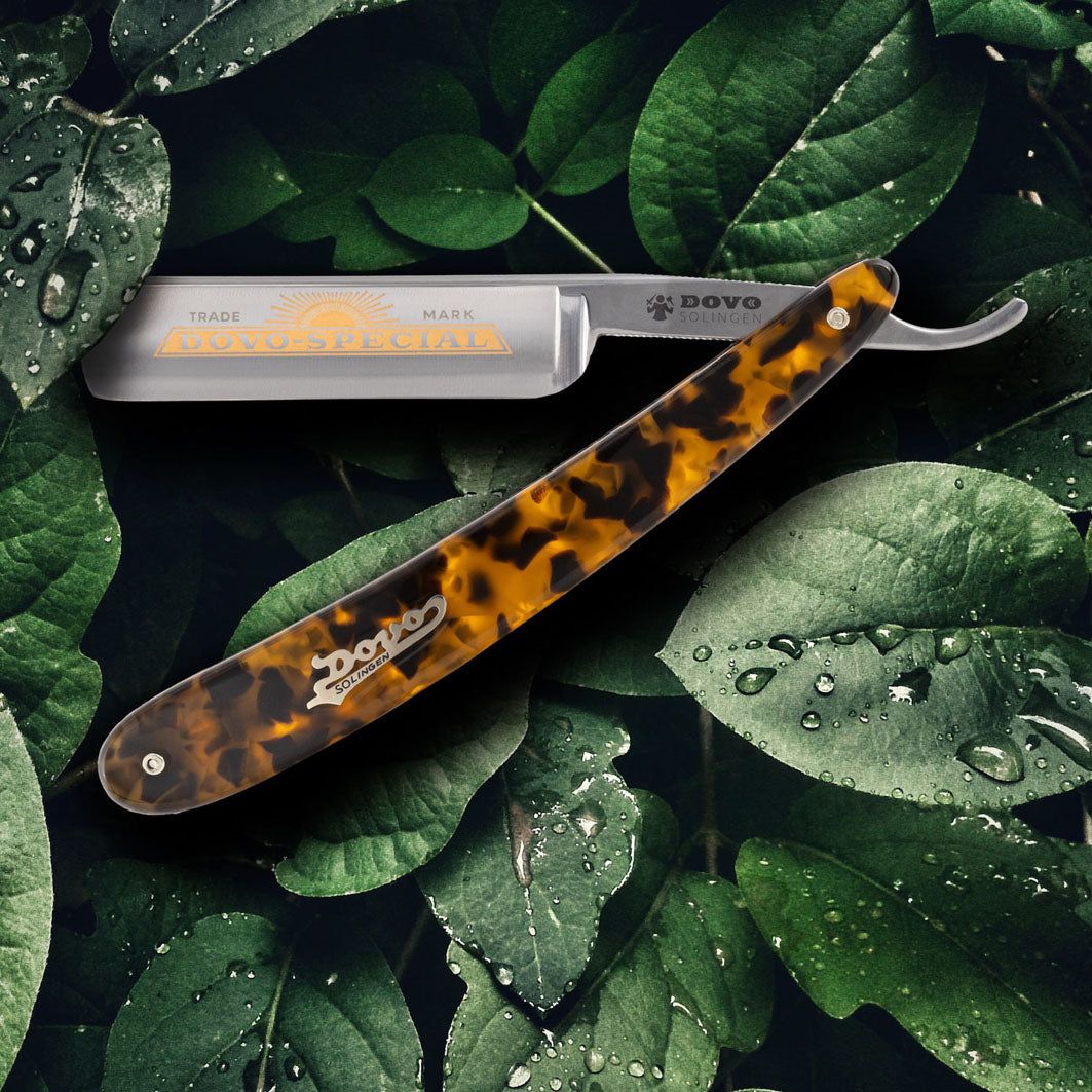 Rasierer mit Griff in Schildpatt-Optik. Klinge mit Logo und Schriftzug DOVO SPÉCIAL. Auf Blättern platziert.