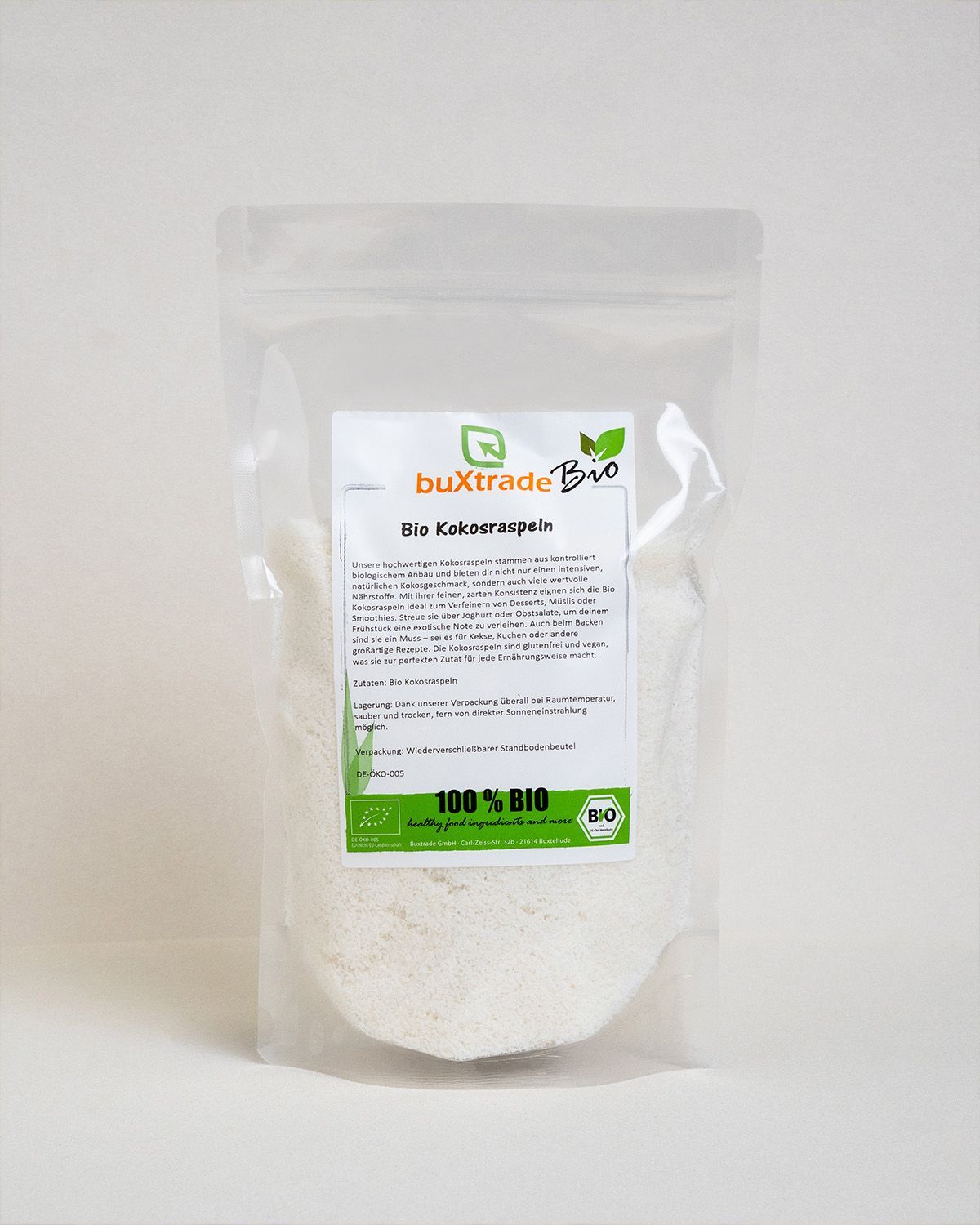 Transparente Verpackung mit buXtrade Bio Kokosraspeln. Text und Bio-Siegel. Weiße Kokosraspeln sichtbar.