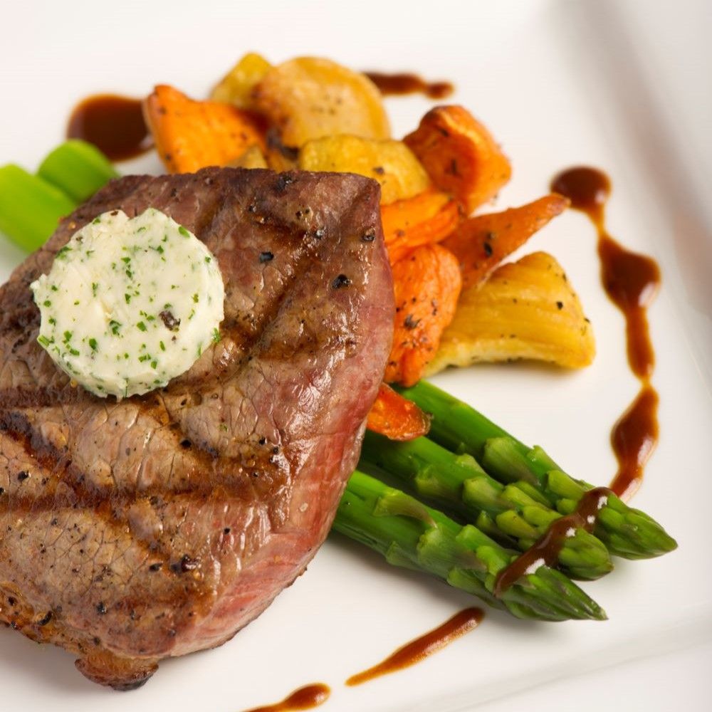 Gebratenes Steak mit Kräuterbutter, Spargel und Gemüse auf weißem Teller. Soße dekoriert das Gericht.