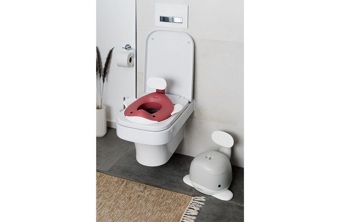 Toilettensitz in Walform auf Toilette. Zweiter Sitz daneben. Wand mit Papierrolle und Dekoration.