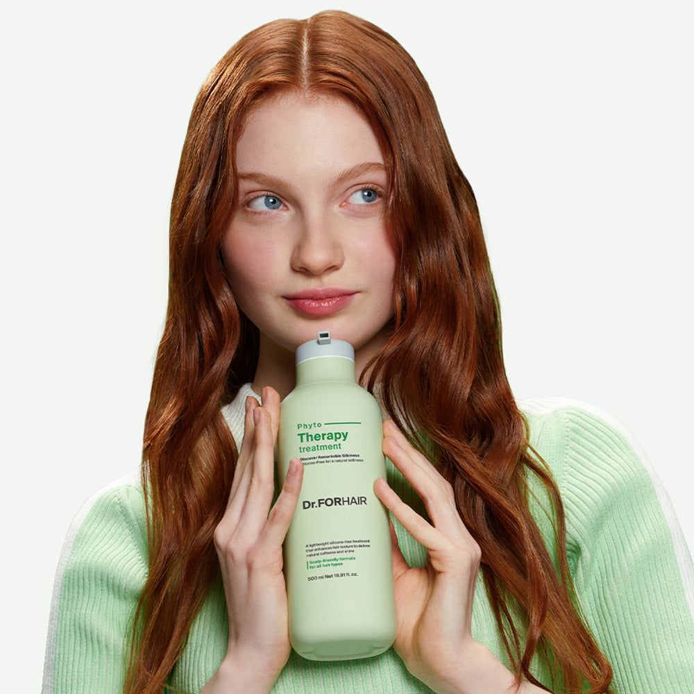 Eine Frau mit roten Haaren hält eine hellgrüne Flasche Dr.FORHAIR Phyto Therapy Treatment vor sich.