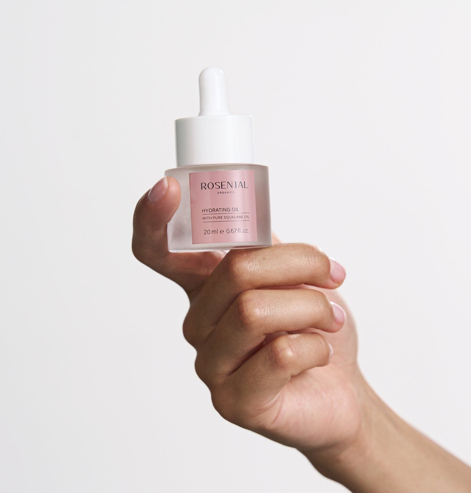 Klarer Glasbehälter mit weißem Deckel. Rosa Etikett mit Text. Wird von einer Hand gehalten.