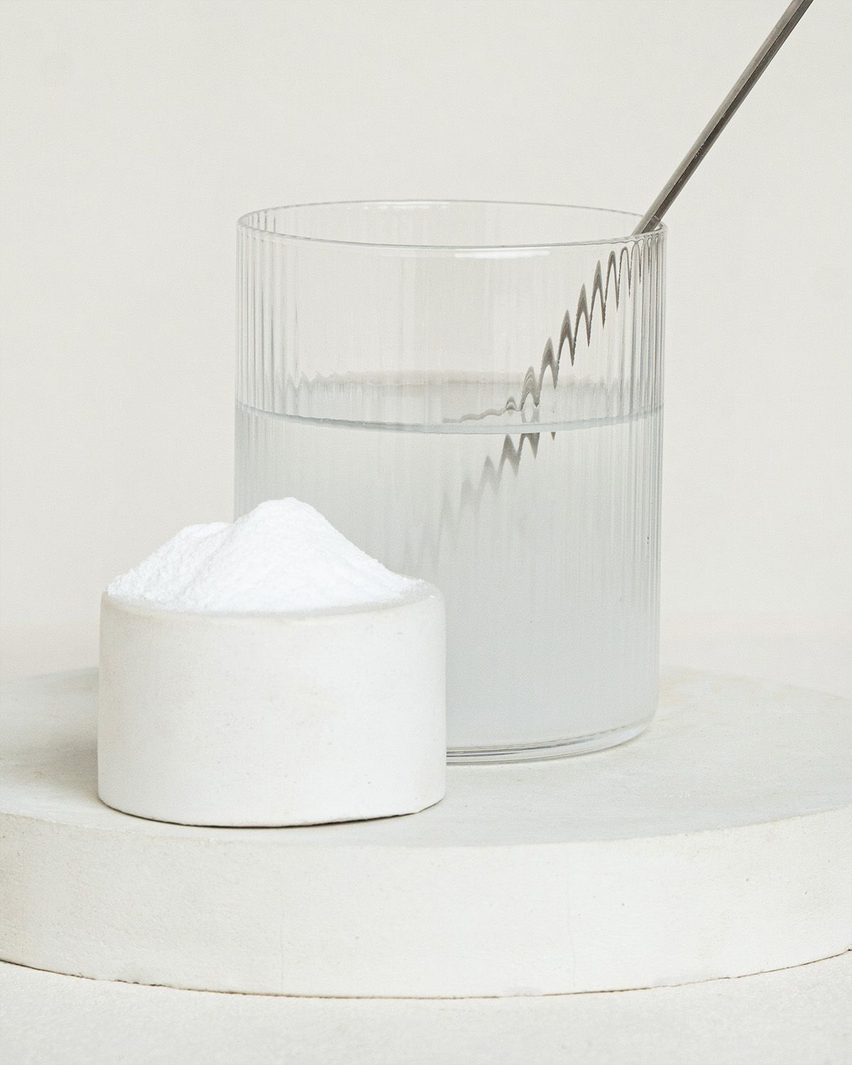 Ein Löffel mit weißem Pulver neben einem Glas Wasser und einem kleinen Behälter mit Pulver.