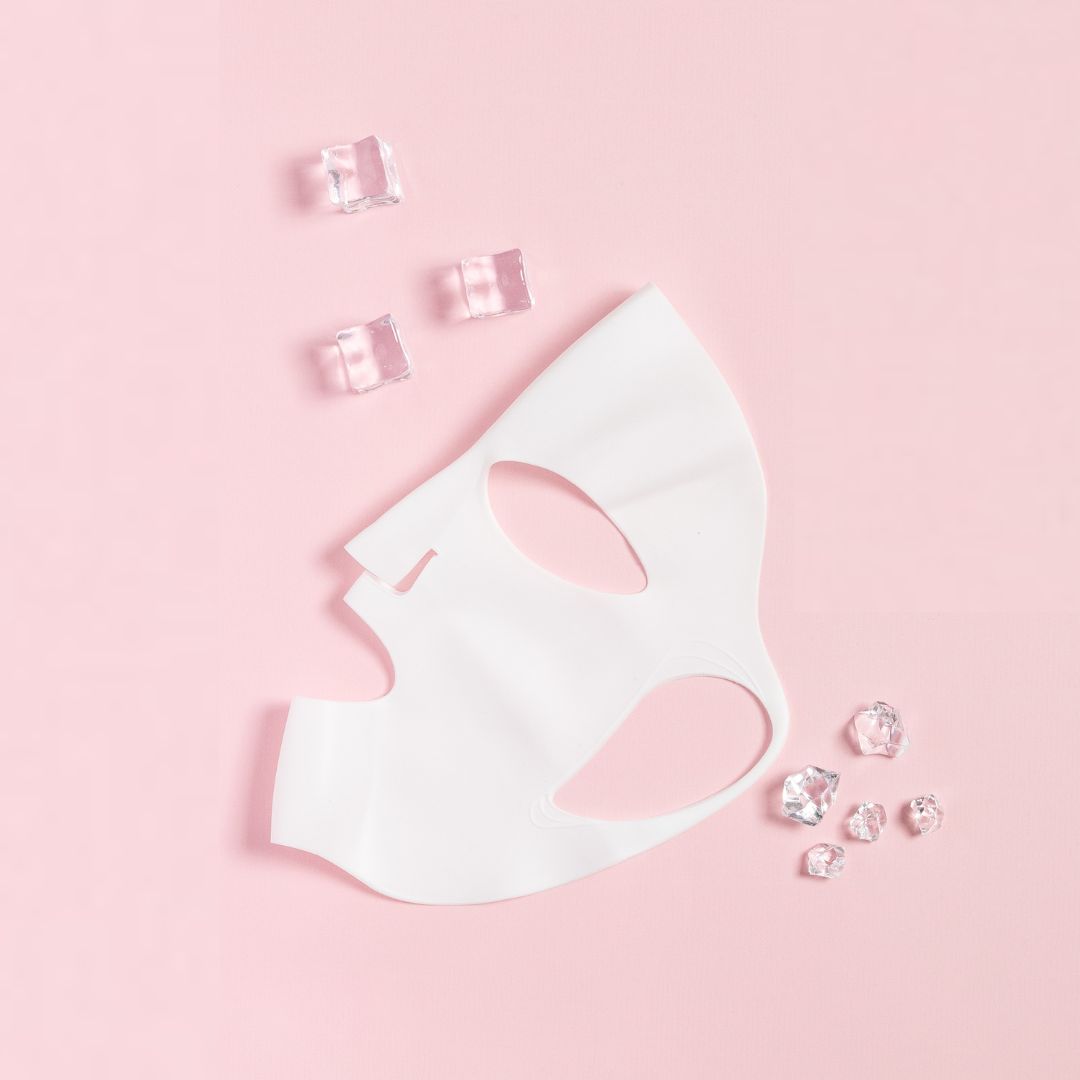 Masque en silicone blanc sur fond rose. À côté, des glaçons. Découpes pour les yeux, le nez et la bouche.