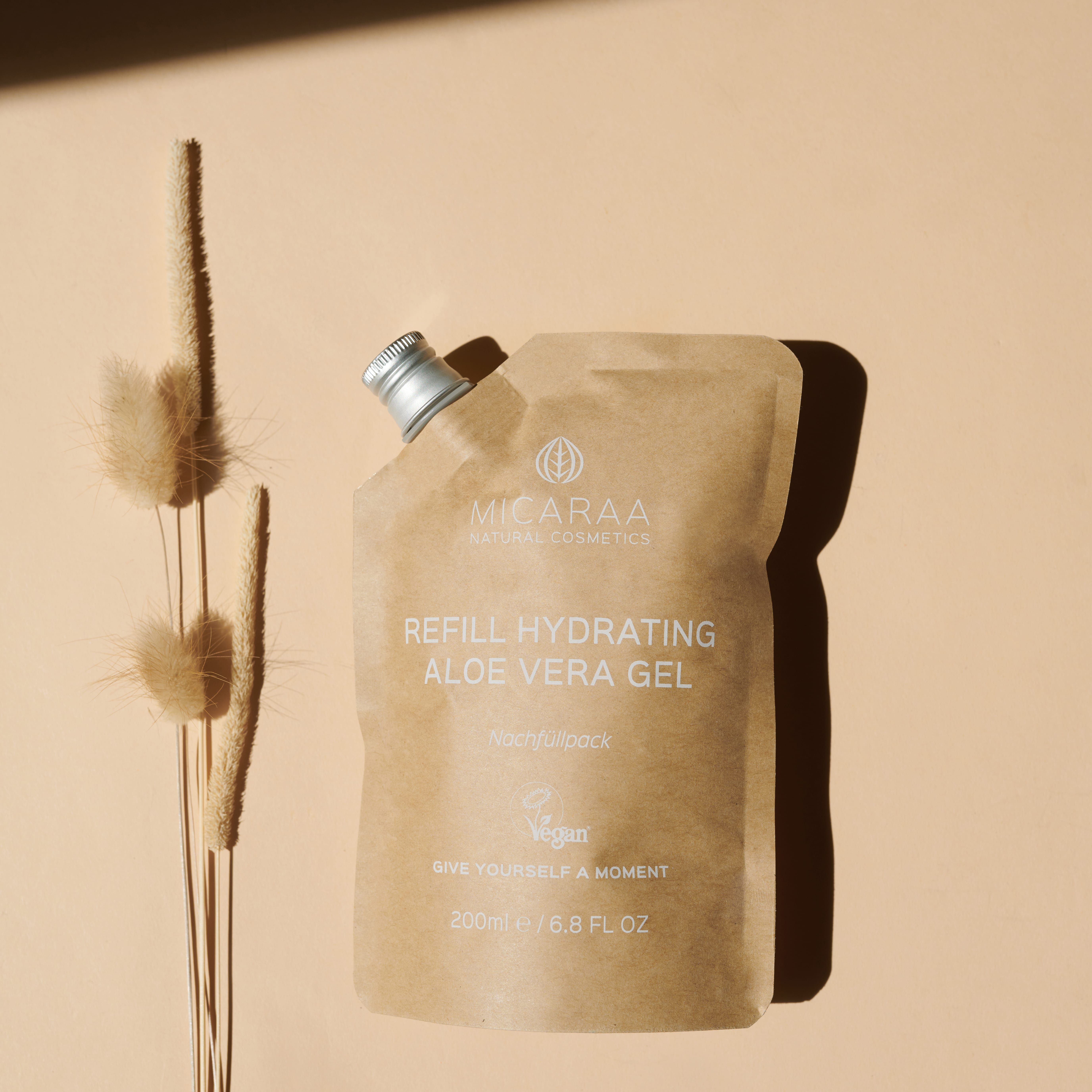 MICARAA Aloe Vera Gel Nachfüllpackung. Braune Papierverpackung mit silbernem Verschluss. Trockenblumen daneben. Text: REFILL HYDRATING ALOE VERA GEL.
