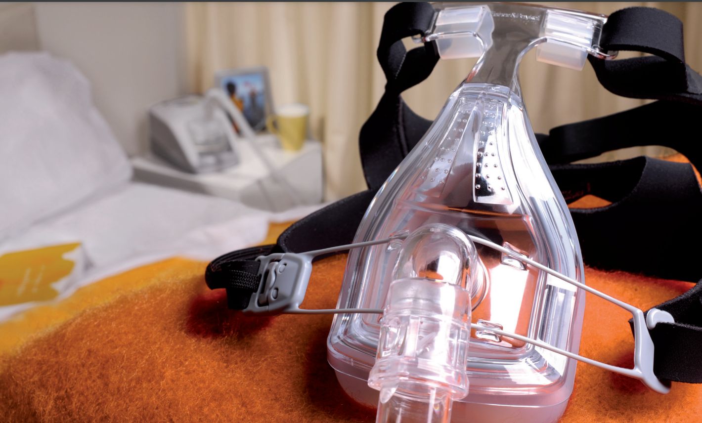 Schlaftherapie-Vollgesichtsmaske aus transparentem Material mit schwarzem Kopfband, auf einem orangefarbenen Stoff.