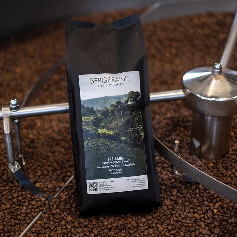 Schwarzer Beutel mit BERGBRAND-Logo und Produktinformationen. Kaffeebohnen liegen im Hintergrund.