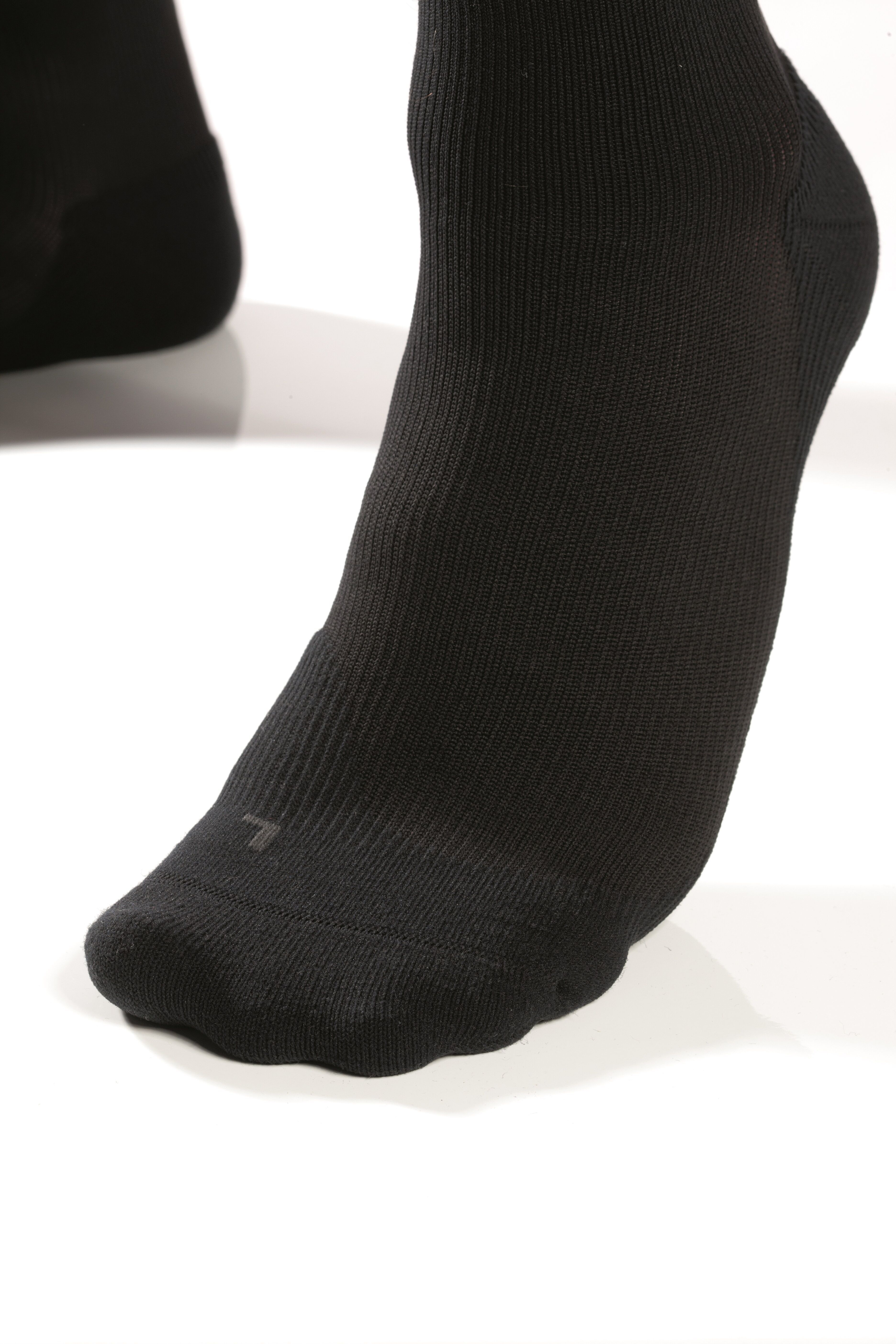 Schwarze Socke mit Rippenmuster, die einen Fuß bedeckt. Ein kleines 'L' ist auf dem Zehenbereich sichtbar.