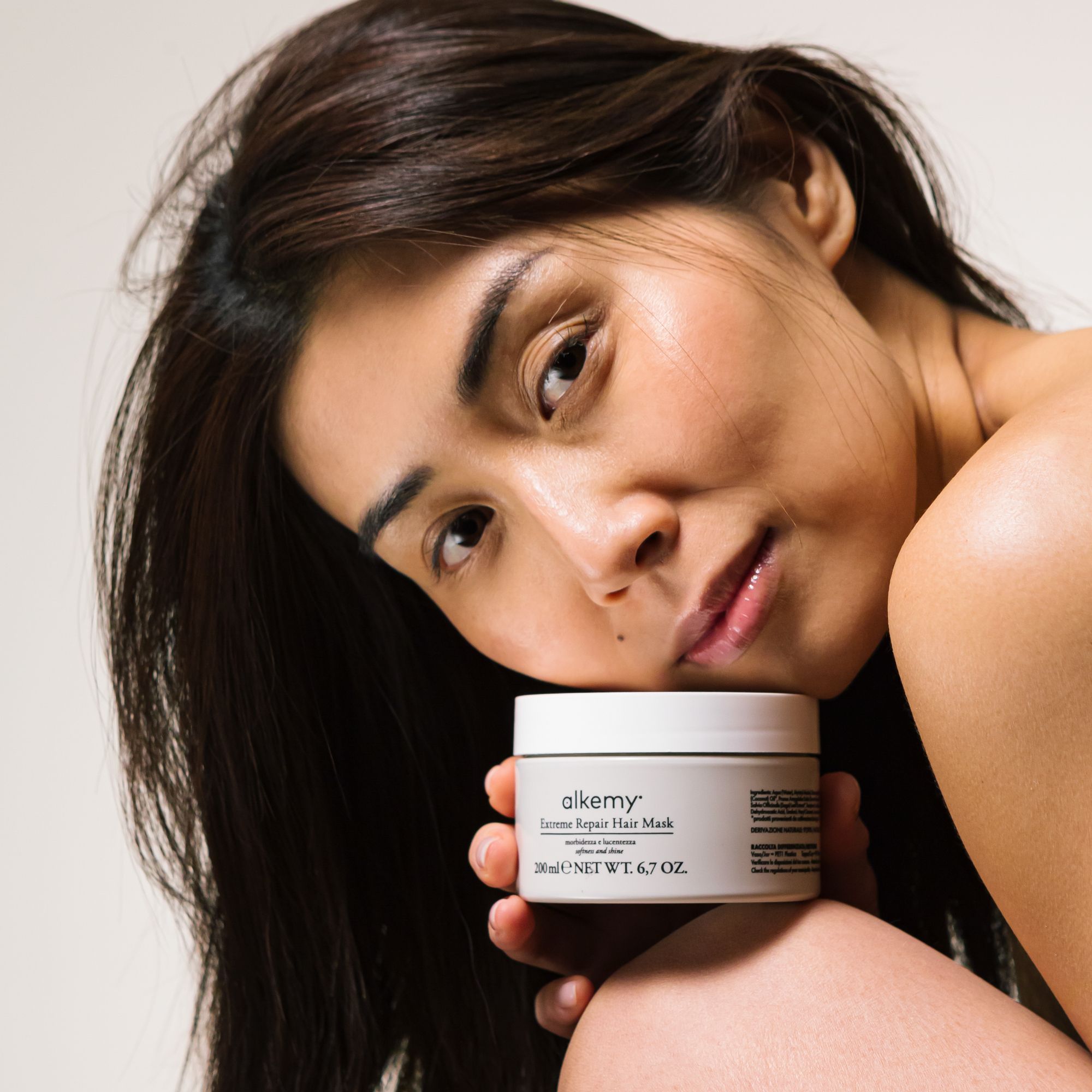 Alkemy Intense Repair Haarmaske in einem cremefarbenen Tiegel, gehalten von einer Frau.