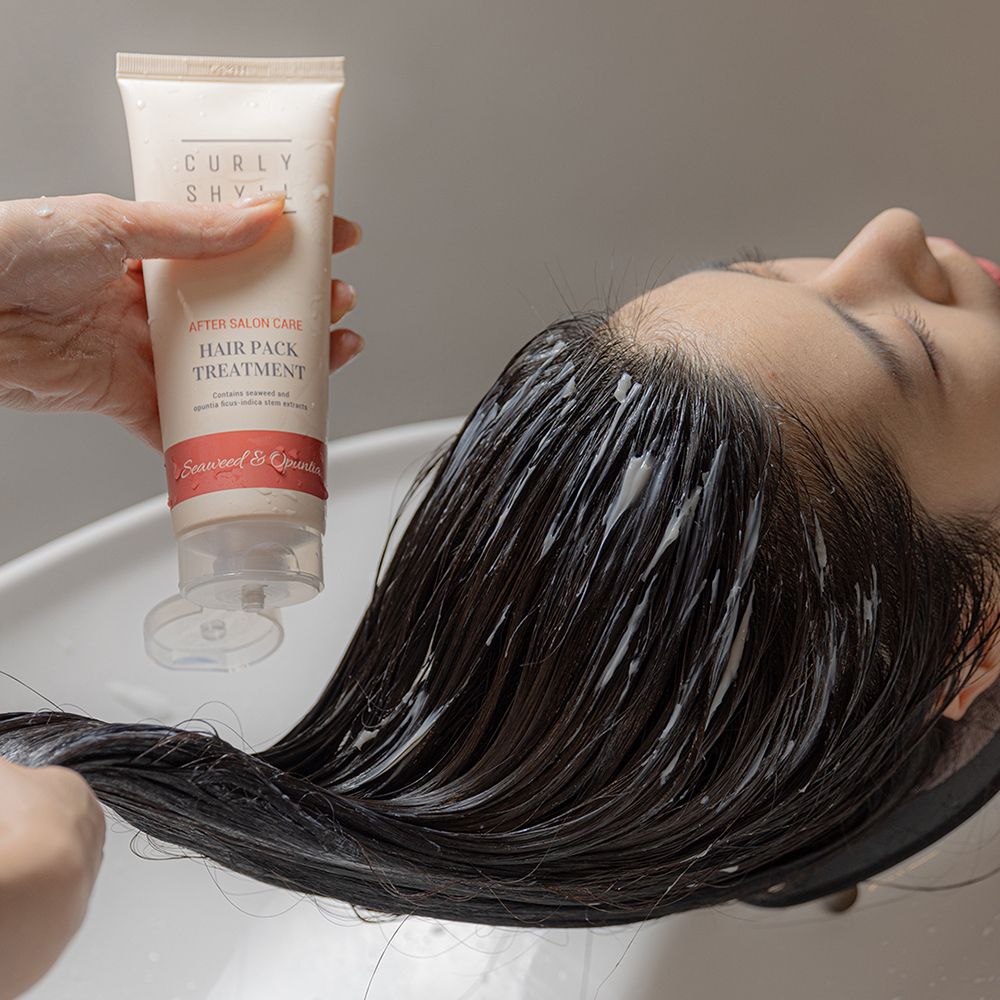 Person mit Haaren, die mit einer Creme behandelt werden. Tube mit Produktnamen.
