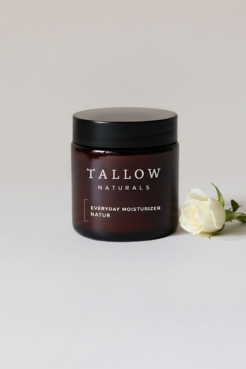 Braunes Glas mit schwarzem Deckel. Aufschrift: TALLOW NATURALS, darunter: EVERYDAY MOISTURIZER. Daneben eine weiße Rose.