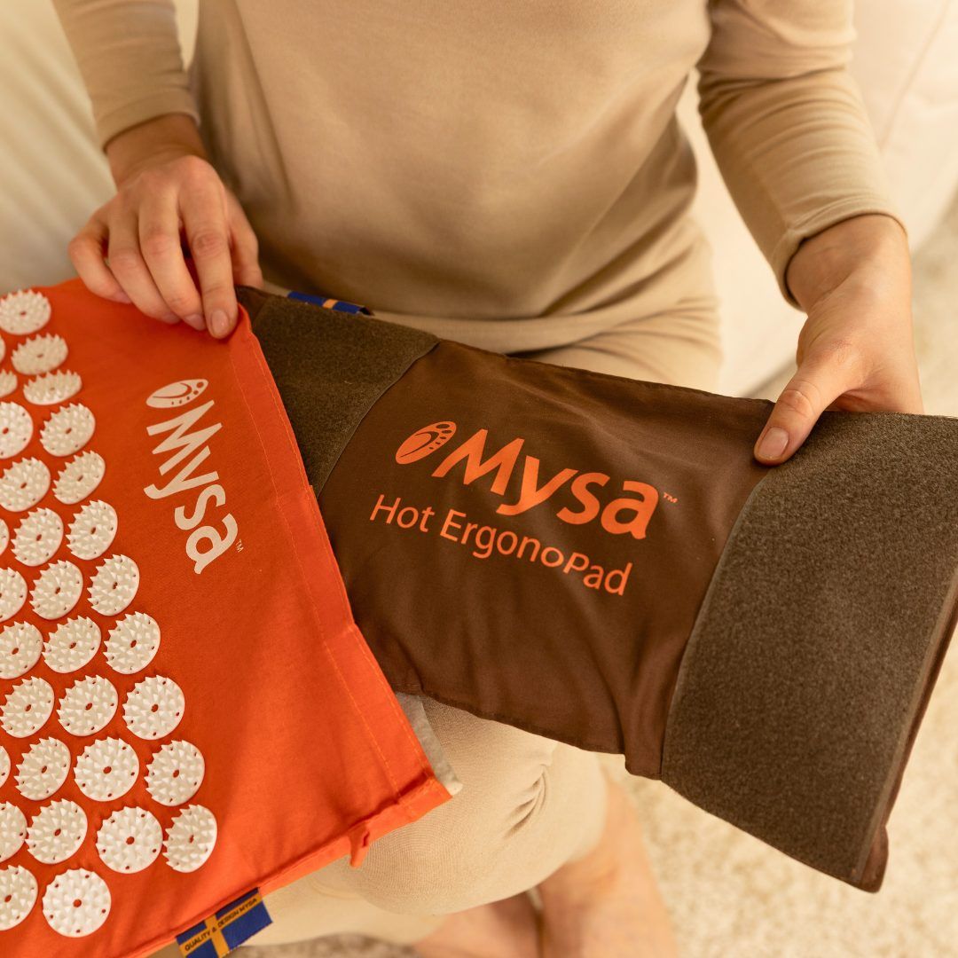 Hände halten ein orangefarbenes Kissen mit weißen Noppen und ein braunes Kissen. Beide haben das Mysa-Logo.