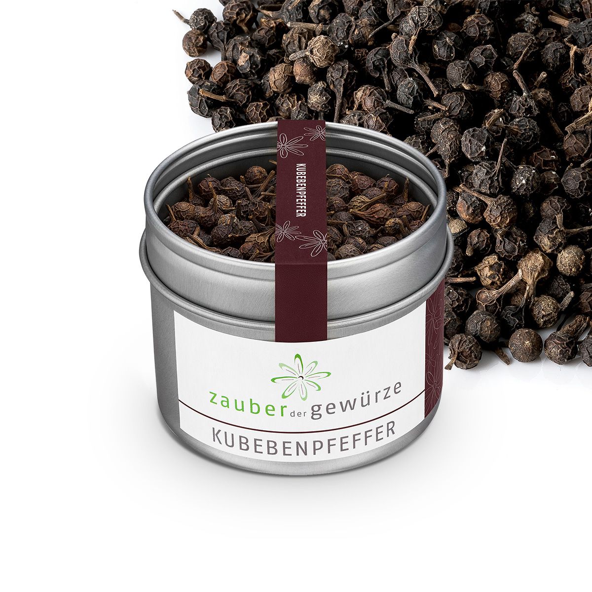 Geöffnete, silberne Dose mit Kubebenpfeffer. Weißes Etikett mit 'Zauber der Gewürze' und 'Kubebenpfeffer'. Dunkelrotes Band. Pfefferkörner daneben.