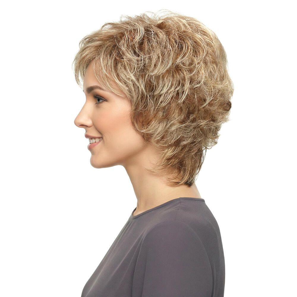 Kurzhaarperücke mit gewelltem Haar in Blondtönen. Seitenansicht einer Frau mit grauer Bluse. Der Hintergrund ist weiß.