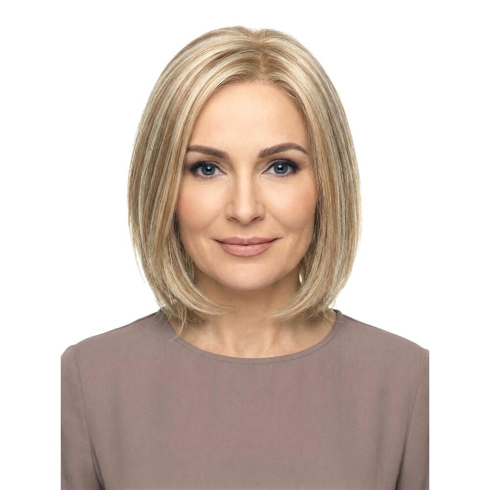 Blonde Perücke mit kurzen, gestuften Haaren. Frontale Ansicht einer Frau mit der Perücke. Hellbraunes Oberteil.