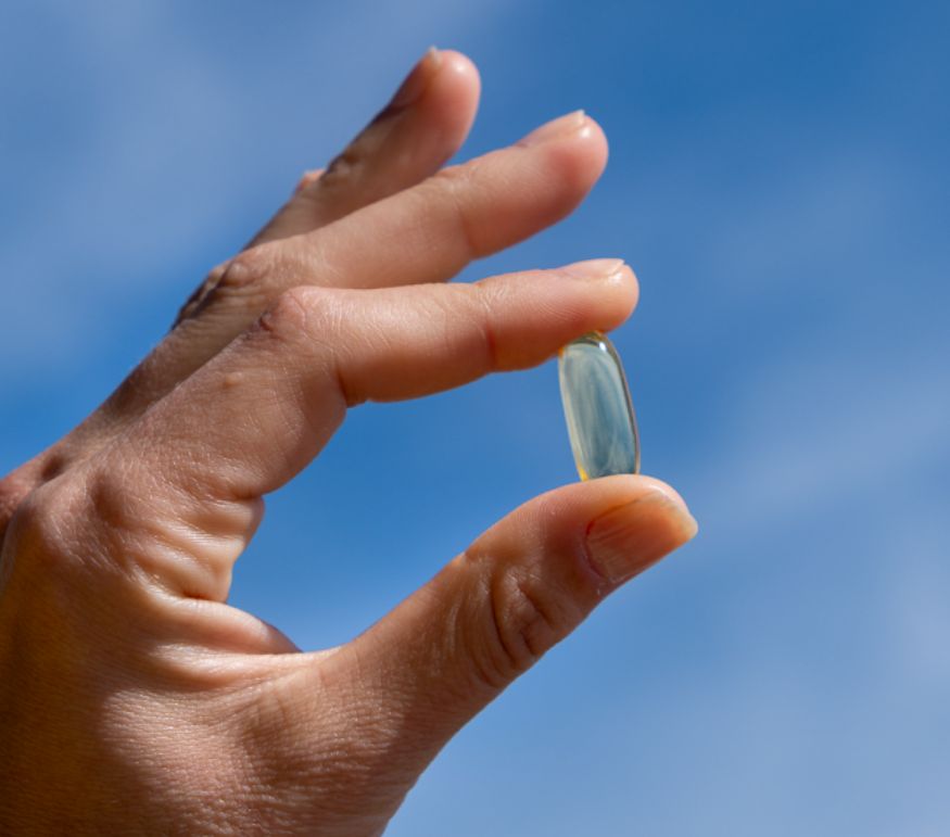 Hand hält eine Aavalabs Omega-3 Fischöl-Weichkapsel vor blauem Himmel.
