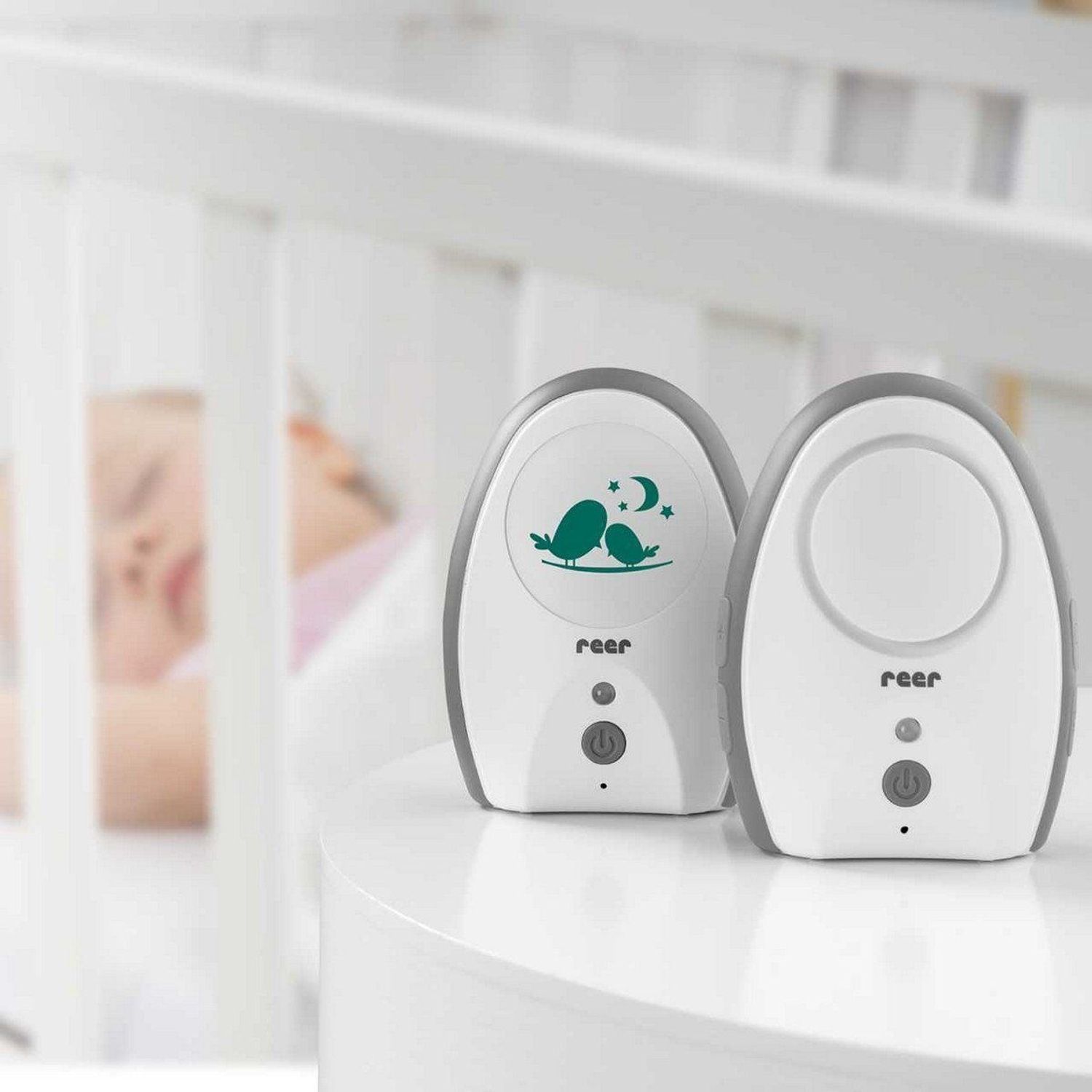 Ein Babyfon steht auf einem Tisch vor einem Babybett. Ein Baby schläft im Bett.
