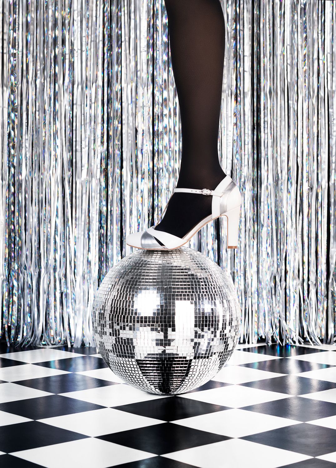 Eine Person steht mit einem Bein auf einer Discokugel. Sie trägt schwarze Strümpfe und einen weißen Schuh.