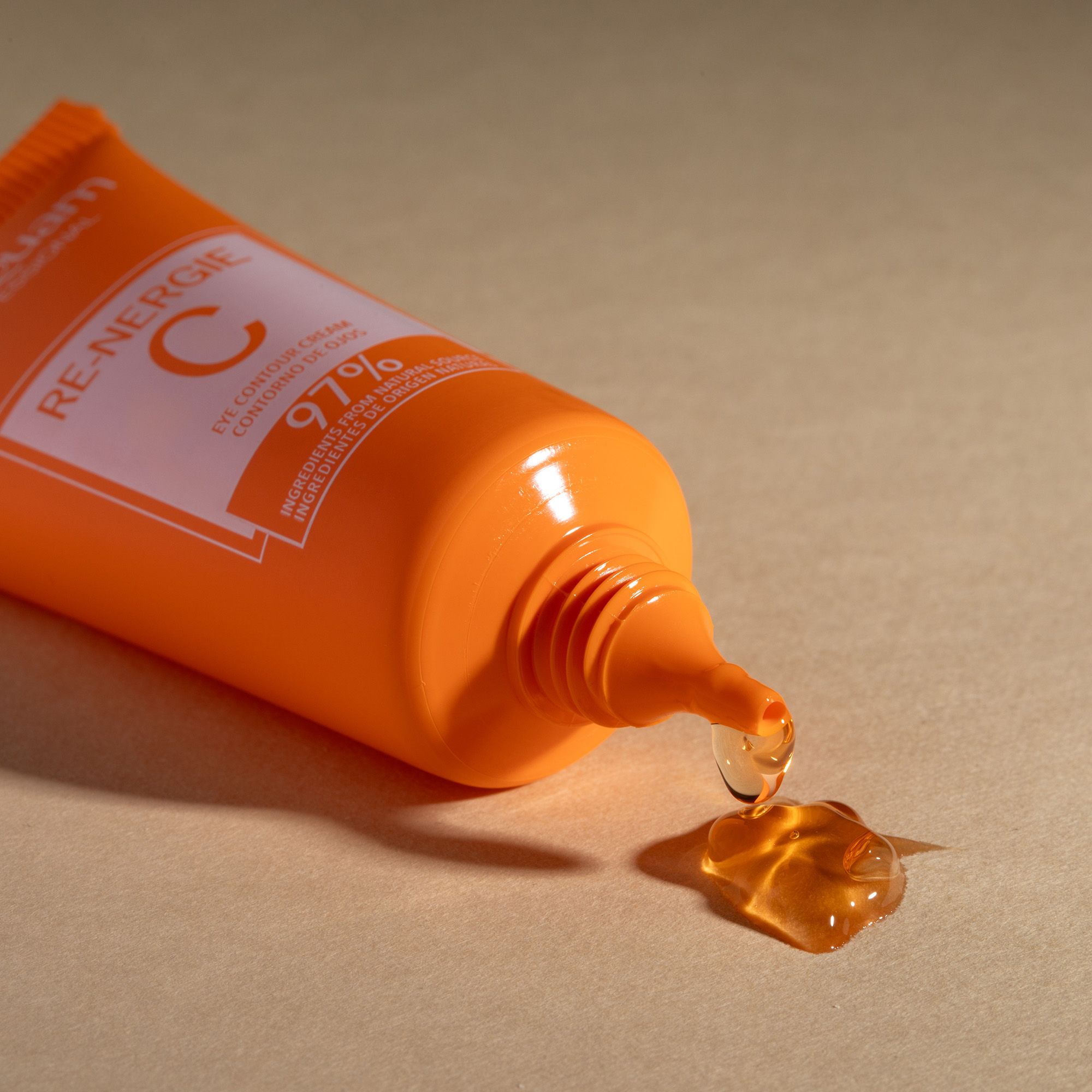 Postquam Re-Nergie C Augencreme. Orange Tube, Produkt tropft. Text: Eye Contour Cream, 97% Inhaltsstoffe natürlichen Ursprungs.