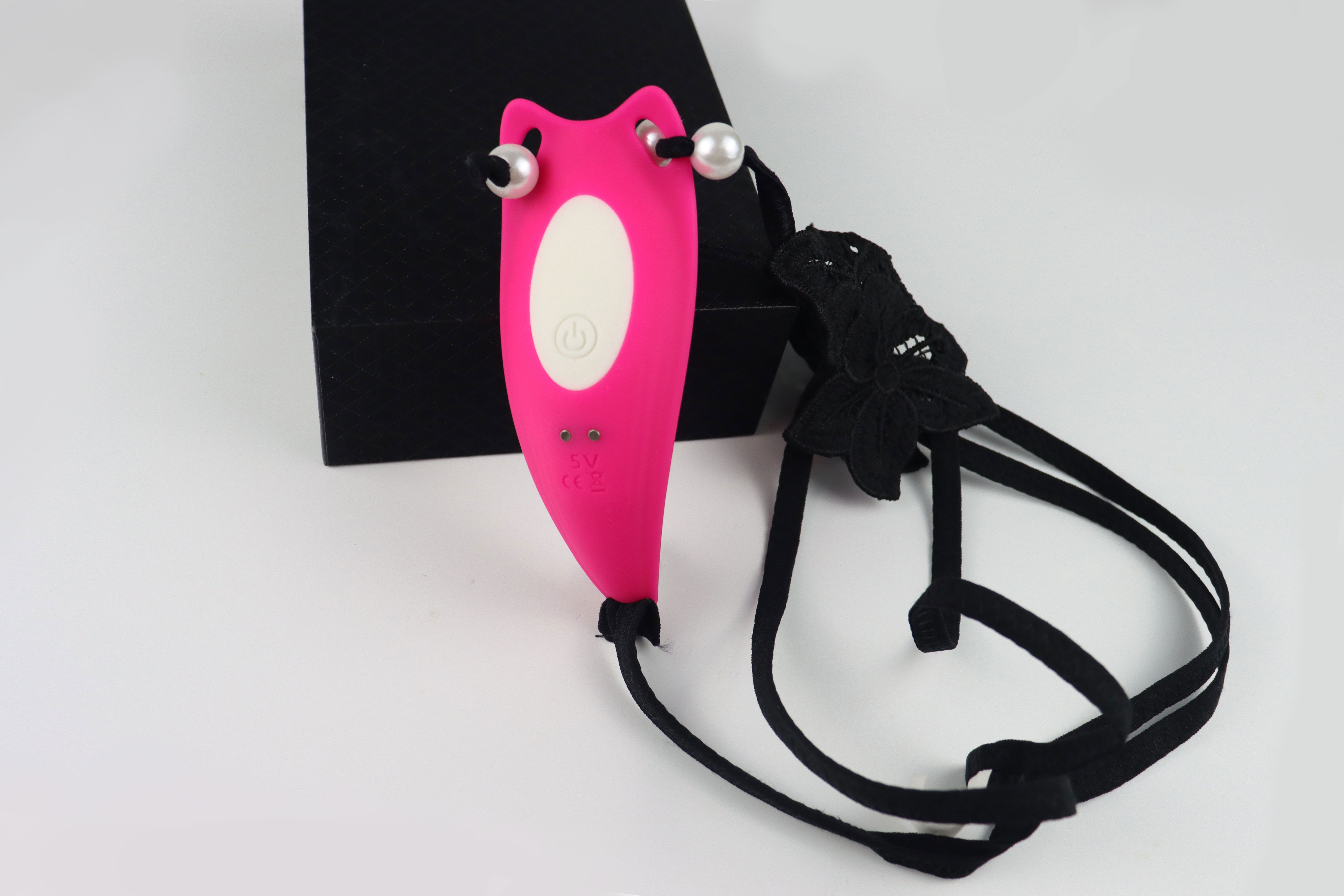 Pinkfarbener Vibrator mit schwarzem Band und Perlen. Auf weißem Hintergrund. Schwarze Geschenkbox.