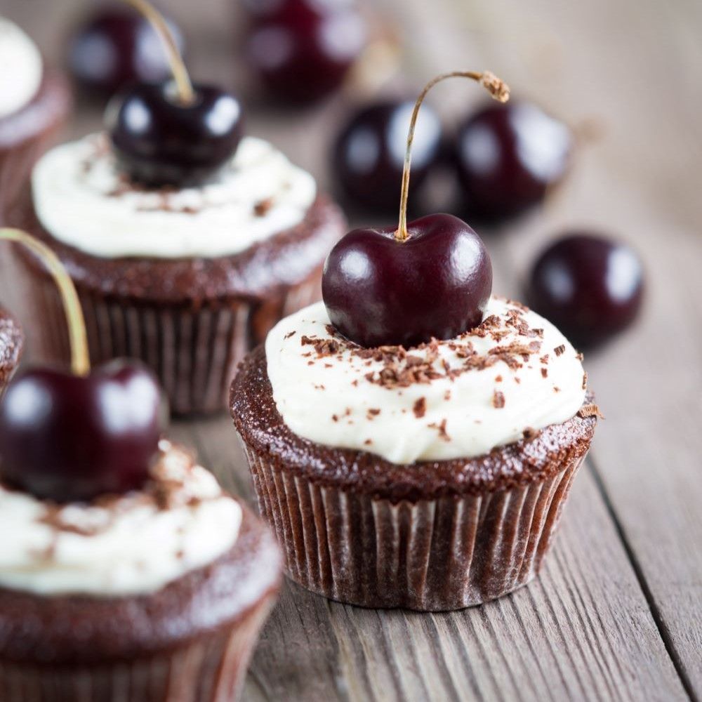 Schokoladen-Cupcakes mit Sahnehaube und Kirsche. Auf Holzuntergrund. Mehrere Cupcakes mit Kirschen dekoriert.