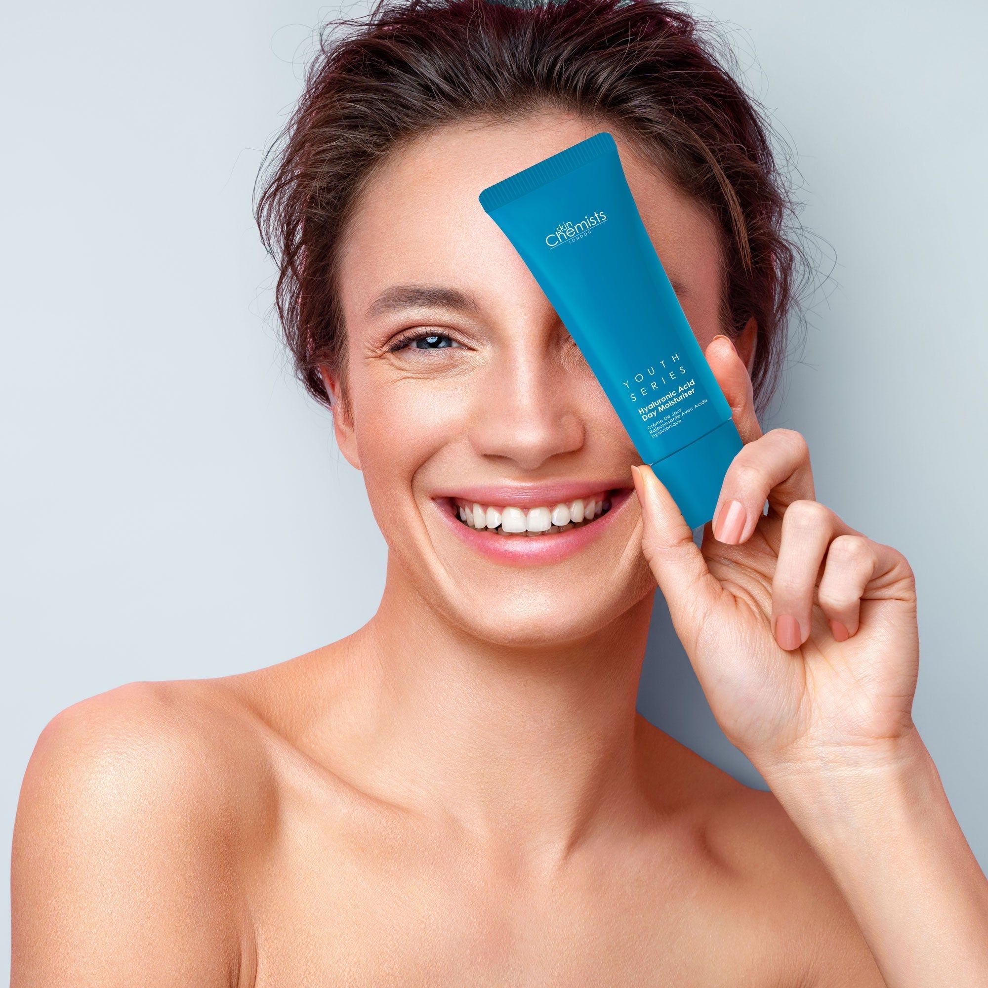 Frau hält blaue Tube vor dem Gesicht. Aufschrift: skinChemists, Youth Series, Hyaluronic Acid Day Moisturiser.