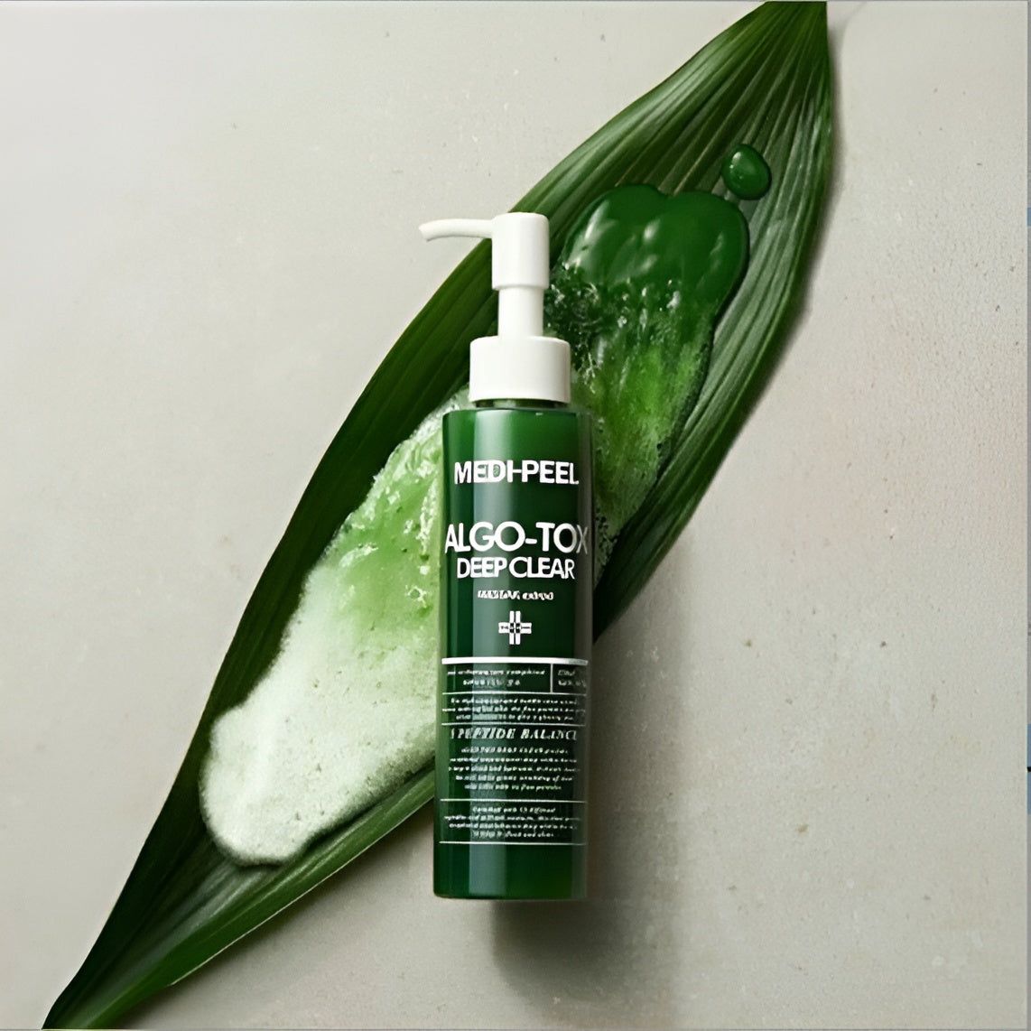 Grüne Flasche mit Pumpkopf auf einem Blatt. Aufschrift: MEDI-PEEL ALGO-TOX DEEP CLEAR. Text und Logo. Schaum.