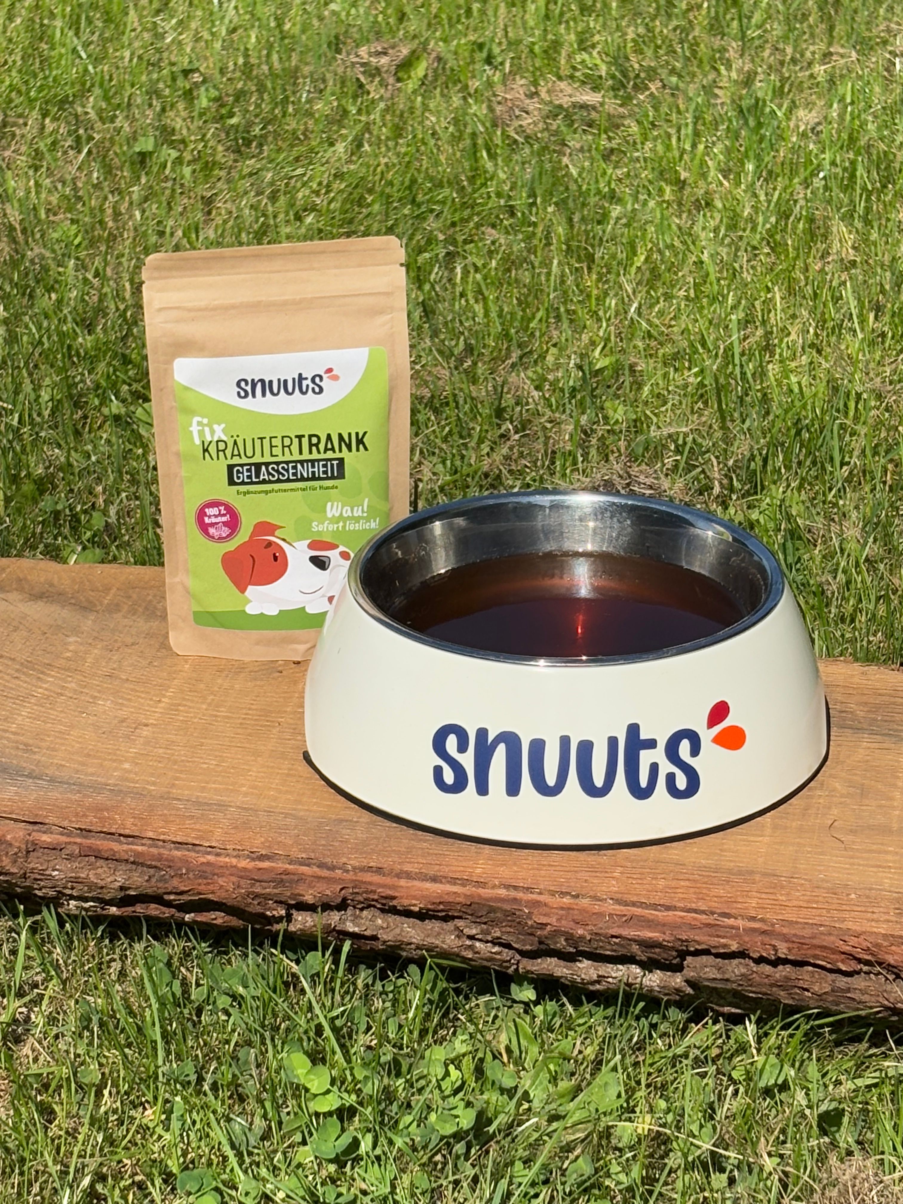 Hundenapf mit Flüssigkeit und braune Tüte. Napf: weiß mit Aufschrift snuuts. Tüte: snuuts Kräutertrank Gelassenheit.