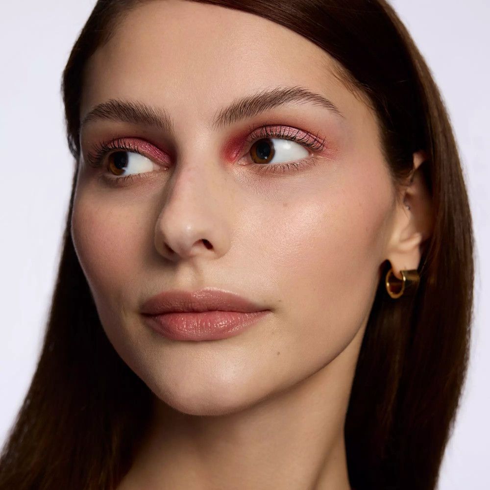 Nahaufnahme einer Frau mit rosafarbenem Lidschatten. Goldene Ohrringe.