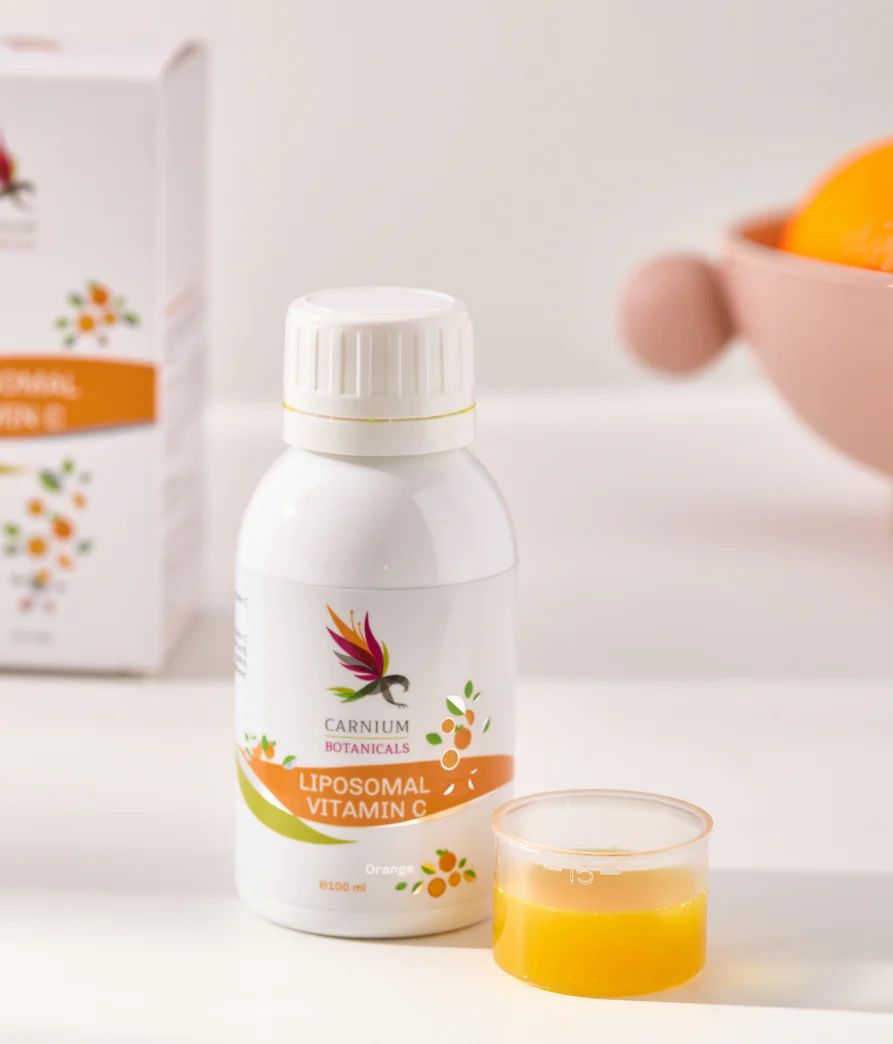 Weiße Flasche mit gelbem Etikett. Carnium Botanicals Liposomales Vitamin C. Messbecher mit Flüssigkeit daneben.