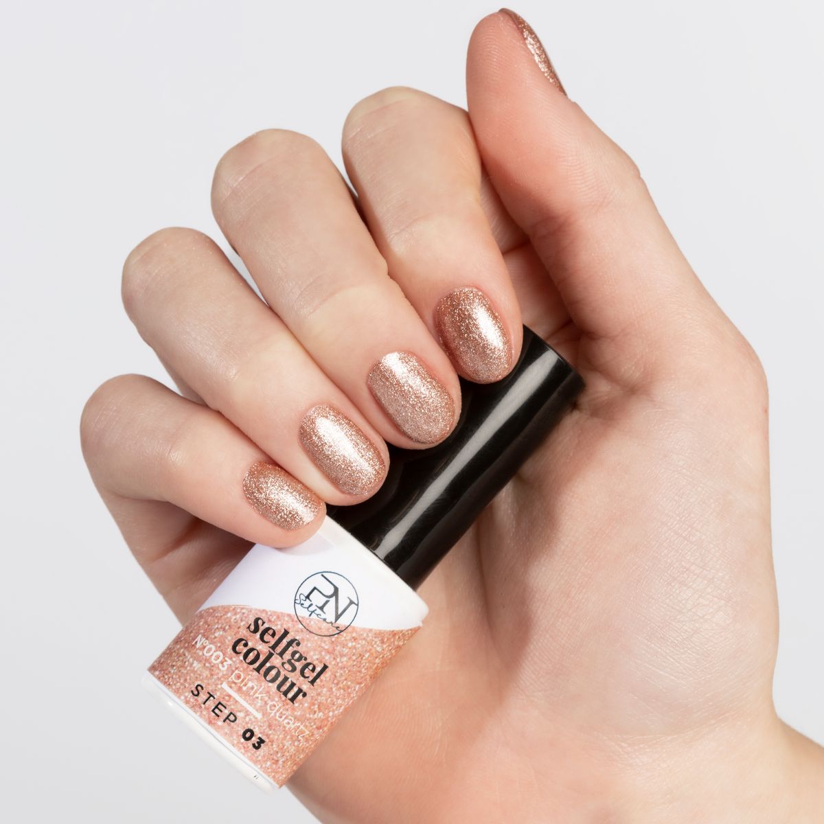 Hand mit lackierten Nägeln in Rosé-Glitzer. Nagellackfläschchen mit schwarzem Deckel. Aufschrift: PN Selfgel Colour.