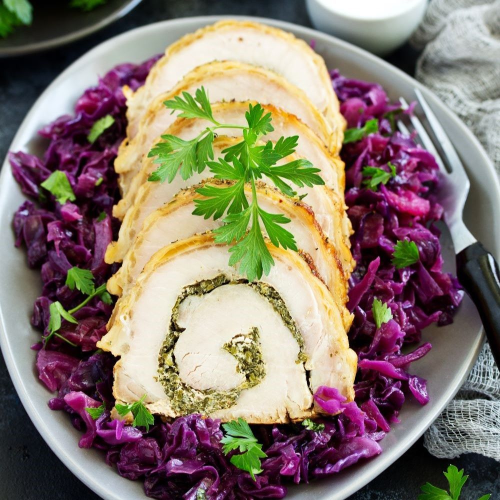 Teller mit Rotkohl und Fleisch. Fleischscheiben auf Rotkohl. Dekoration mit Petersilie. Gabel rechts.