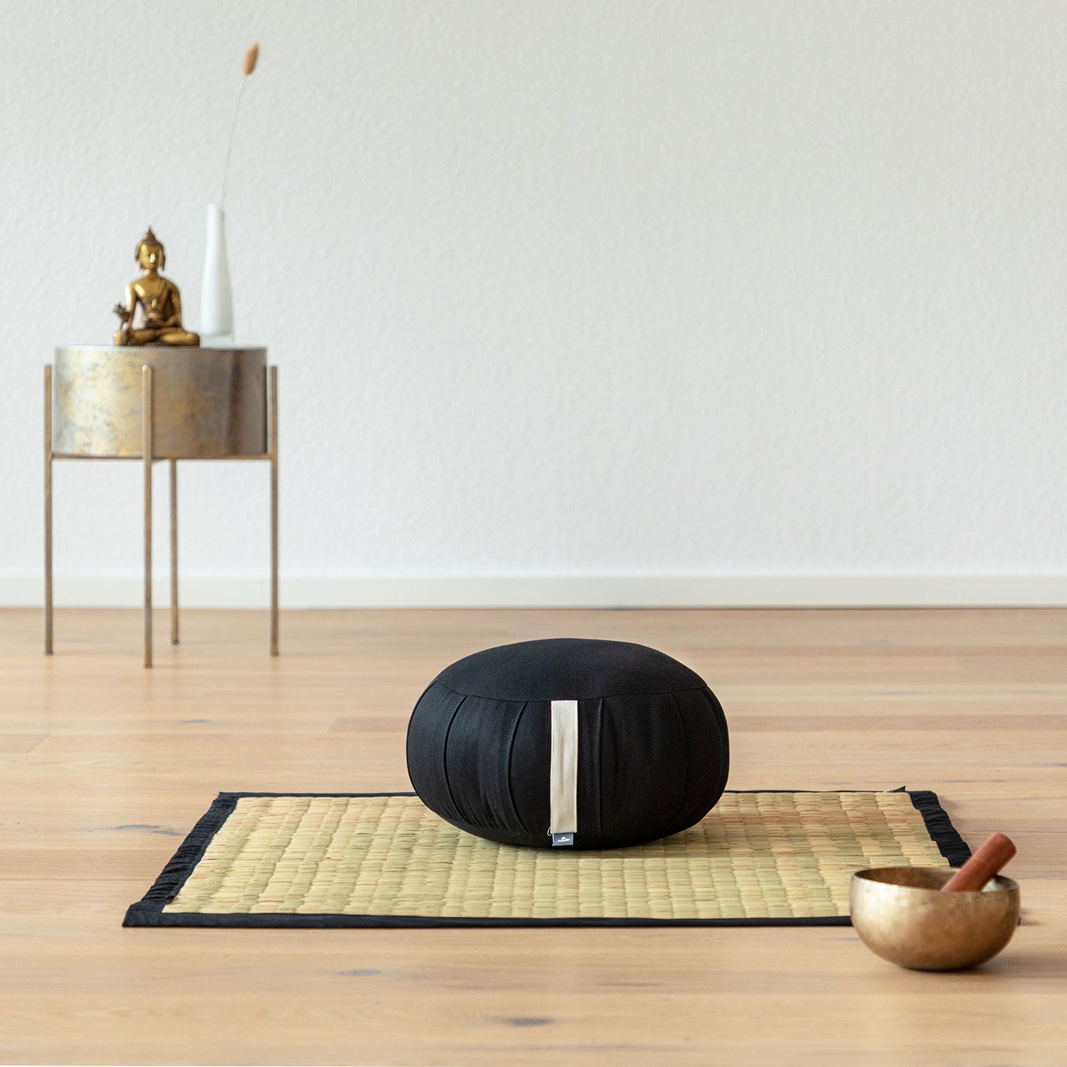 Tatami-Matte mit schwarzem Rand auf Holzboden, daneben ein Kissen und eine Schale.