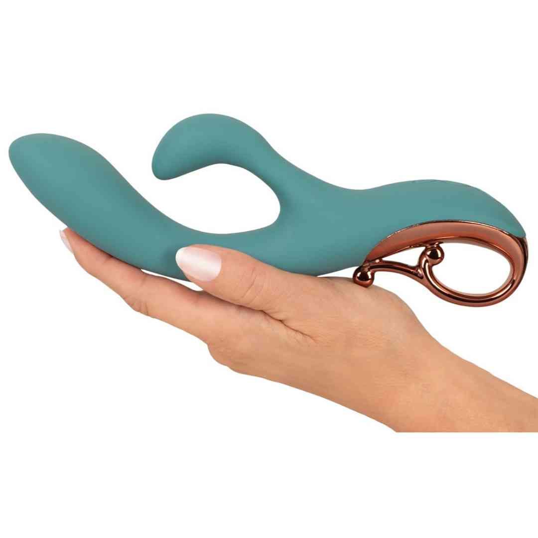 Türkisfarbener Vibrator mit zwei Köpfen und rosegoldfarbenem Griff. Gehalten in einer Hand.