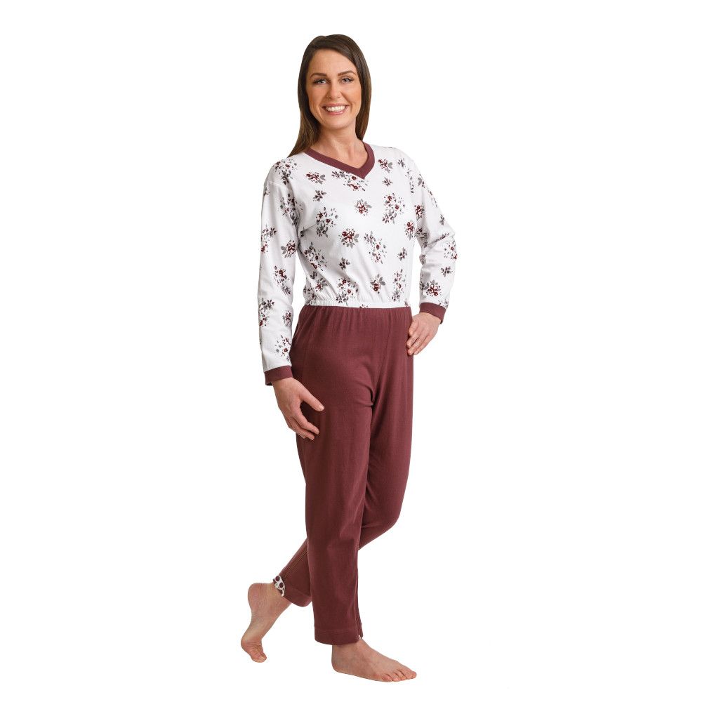 Pflege-Schlafanzug, Aubergine. Zweiteiliger Schlafanzug mit Blumenmuster. Langärmliges Oberteil, V-Ausschnitt, Bündchen. Hose mit Bündchen. Frau trägt den Anzug.