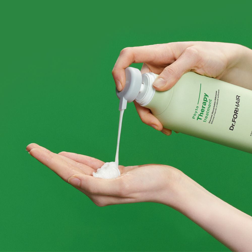 Hände halten eine grüne Flasche und drücken eine weiße Creme heraus. Auf der Flasche steht „Phyto Therapy“ und „Dr. FORHAIR“.