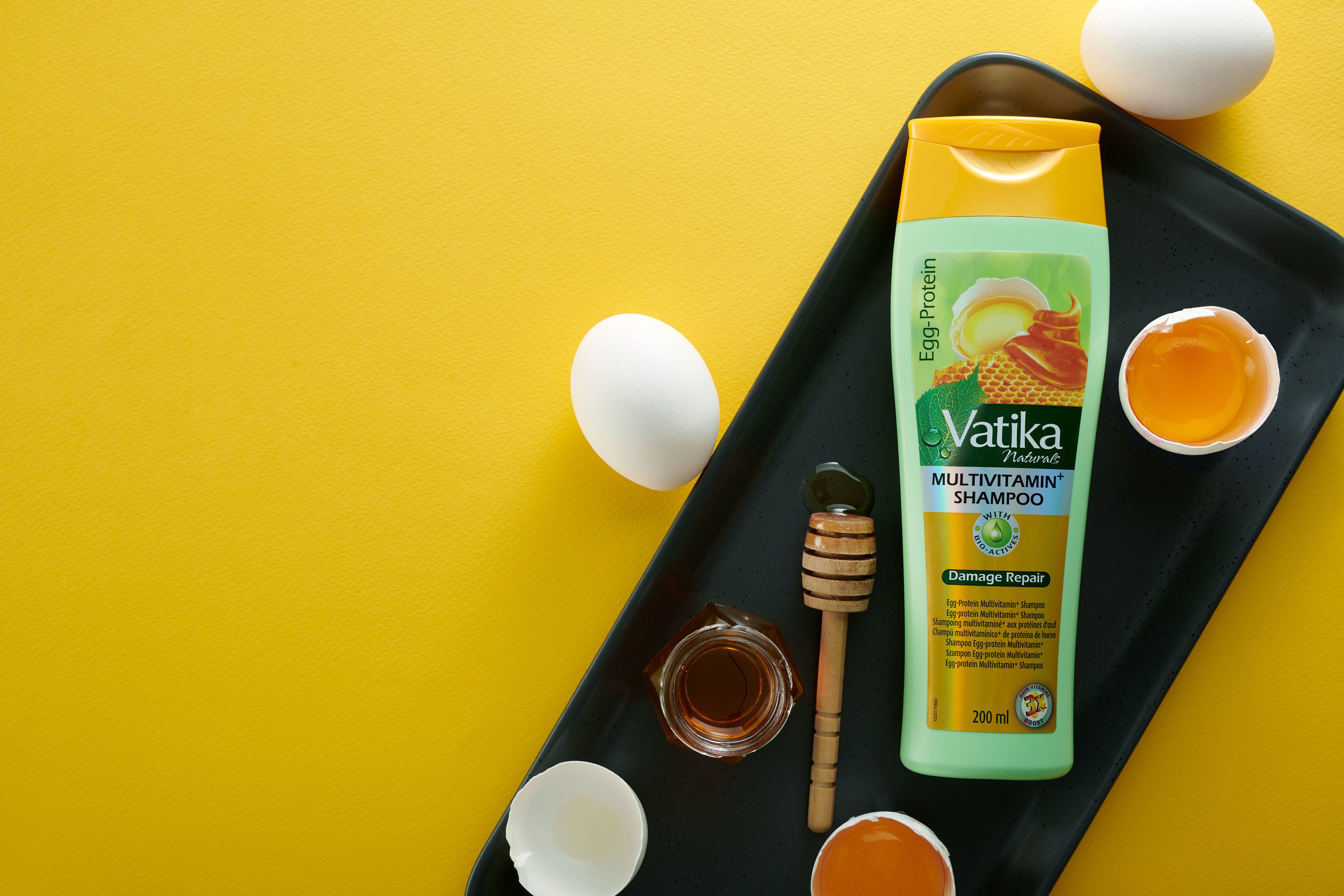 Shampoo-Flasche, Eier, Honig und Löffel auf schwarzem Tablett. Gelber Hintergrund.