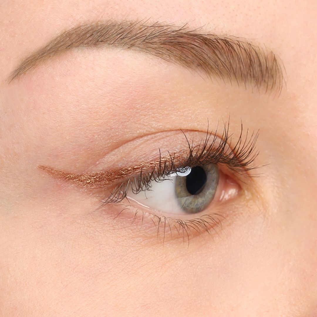 Nahaufnahme eines Auges mit goldfarbenem Kajal-Eyeliner. Der Lidstrich verläuft entlang des oberen Wimpernkranzes.