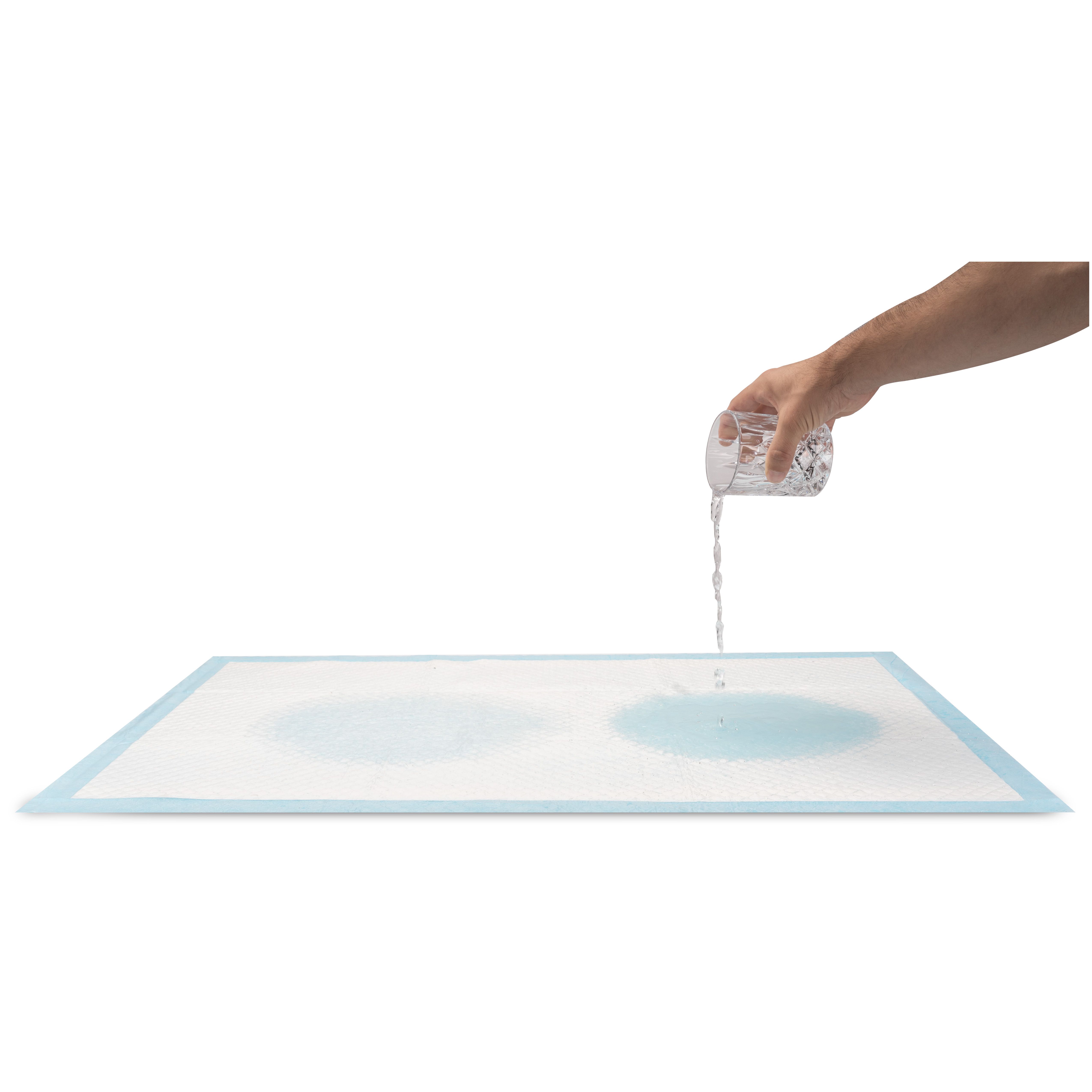 Weiße Einweg-Betteinlage, Wasser wird aus einem Glas gegossen. Zwei nasse Kreise sind sichtbar.