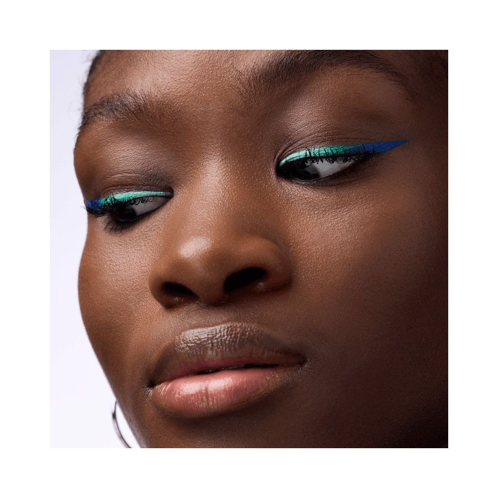 Nahaufnahme einer Frau mit blauem und grünem Eyeliner. Sie trägt Ohrringe.