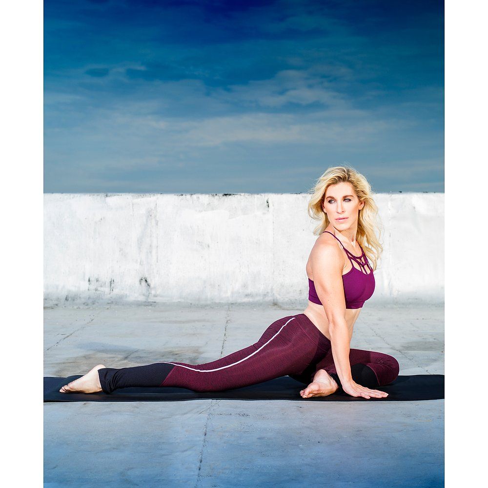 Person in Yoga-Pose auf schwarzer Matte. Person trägt Sport-BH und Leggings. Hintergrund: blauer Himmel und weiße Wand.