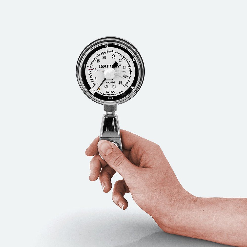 Handdynamometer. Rundes Messgerät mit Anzeige in Pfund. Metallgriff. Hand hält das Gerät.