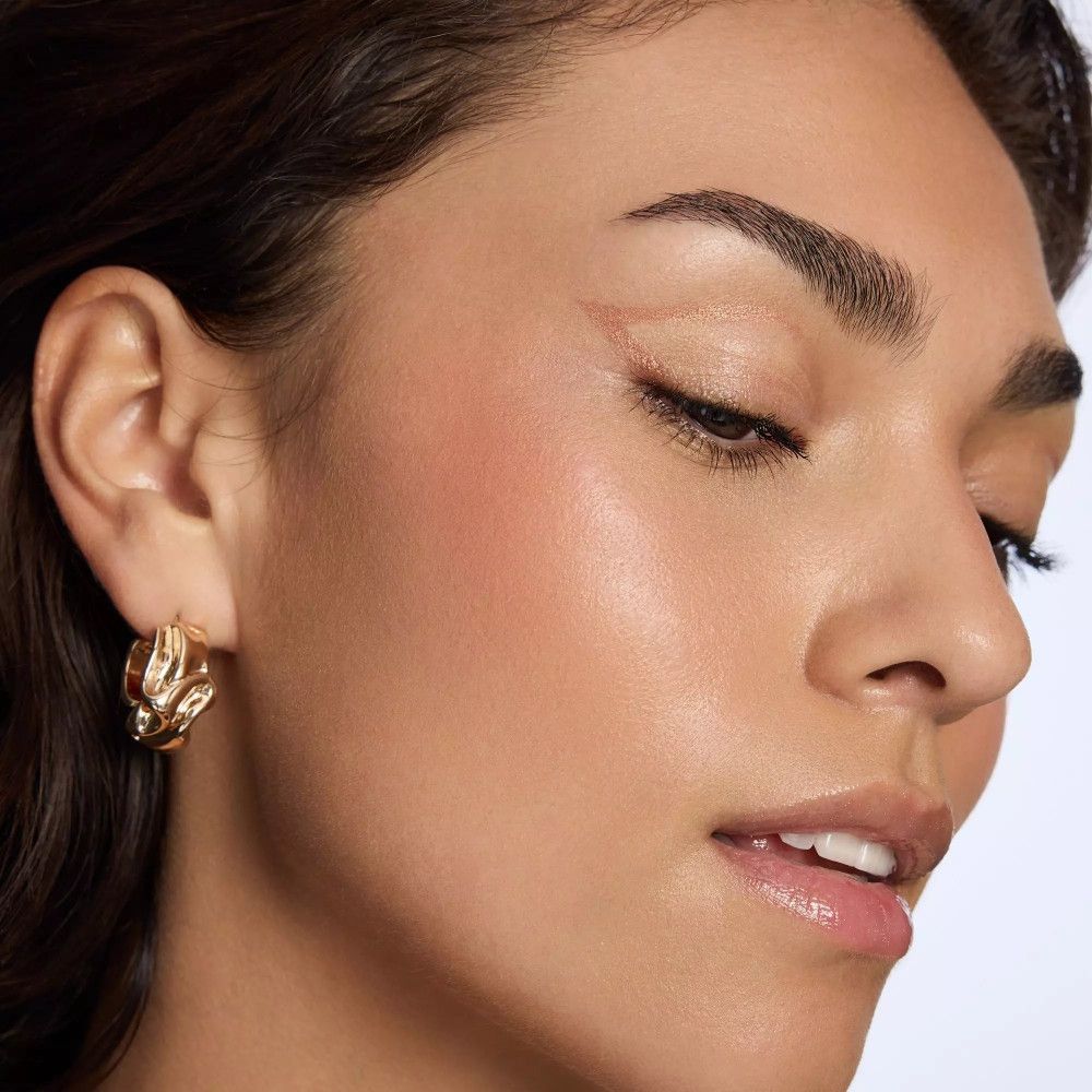 Nahaufnahme einer Frau mit gebräunter Haut. Sie trägt goldene Ohrringe und Make-up.