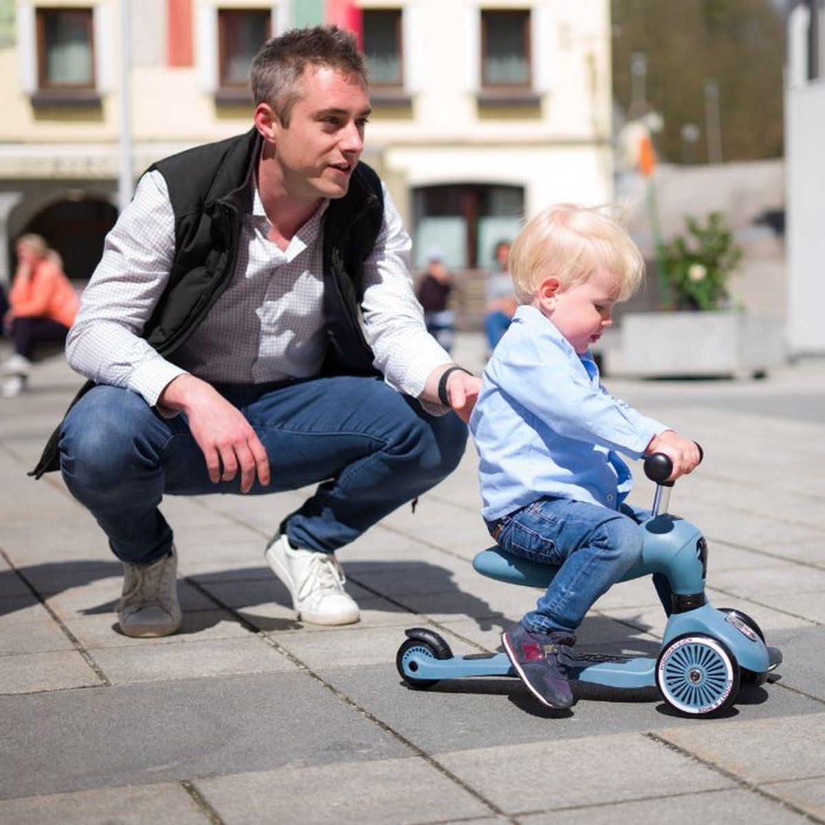 Mann kniet neben einem Jungen auf einem blauen Roller.