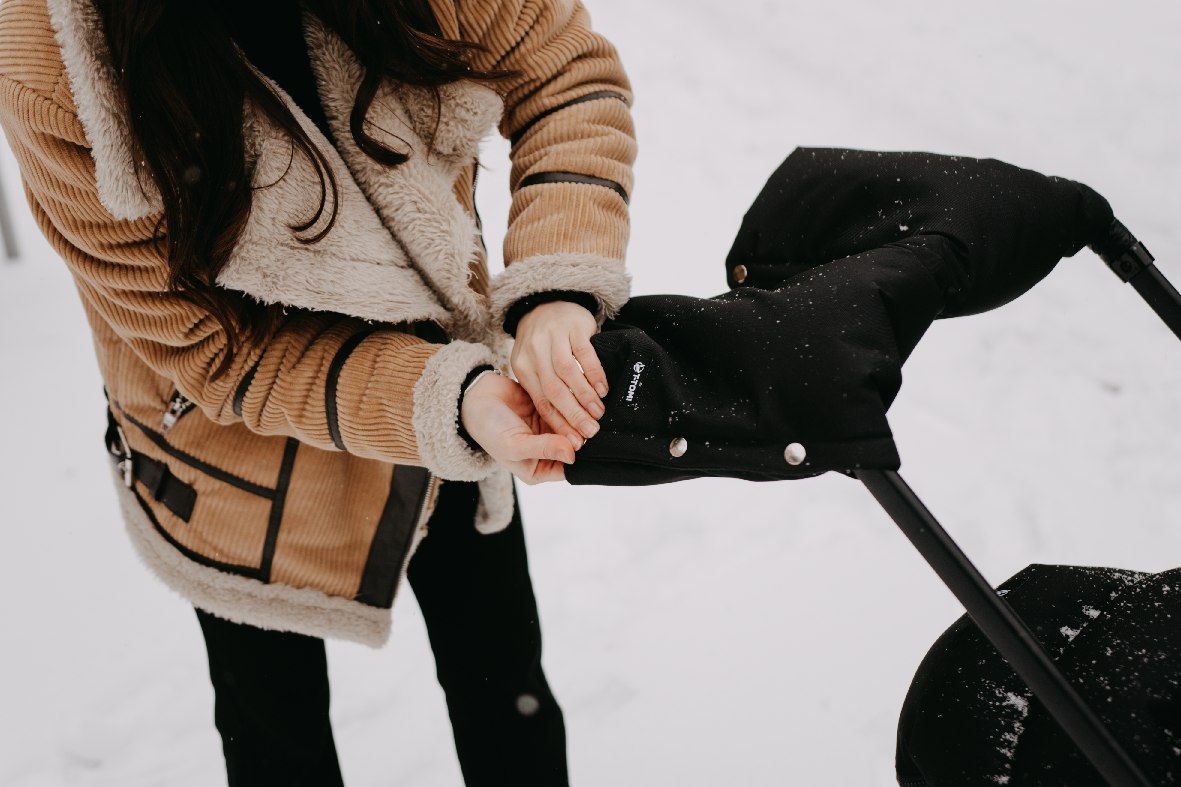 Schwarze, gepolsterte Kinderwagen-Handwärmer mit Druckknöpfen, an einem Griff befestigt.