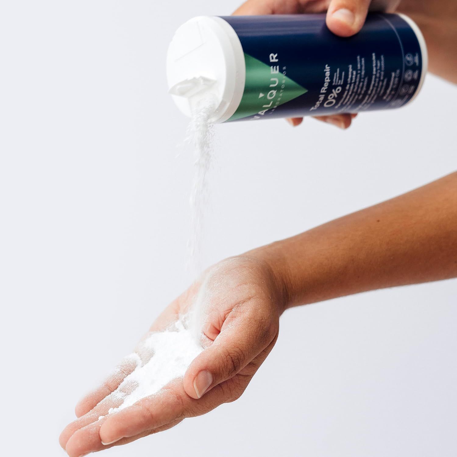 Eine Hand schüttet weißes Pulver aus einer dunkelblauen Flasche "Total Repair" in die andere Hand.