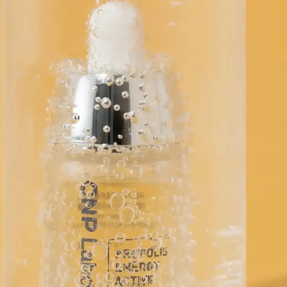 Nahaufnahme einer Flasche mit gelblicher Flüssigkeit und silberner Pipette. Blasen im Hintergrund. Aufschrift: CNP Laboratory, PROPOLIS ENERGY ACTIVE AMPOULE.