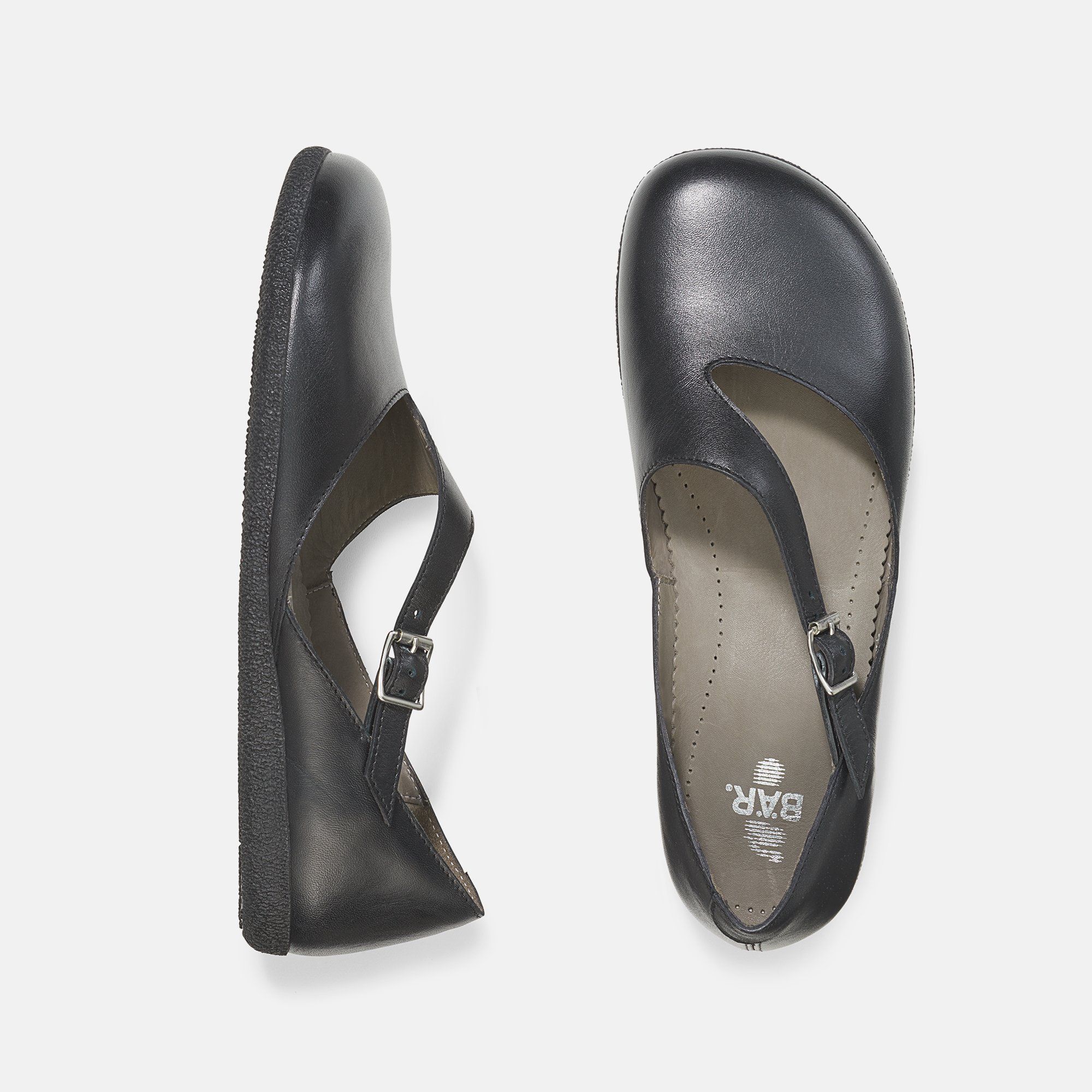 Zwei schwarze Ballerinas. Flache Sohle, Riemen mit Schnalle. Eine von oben, eine von der Seite.