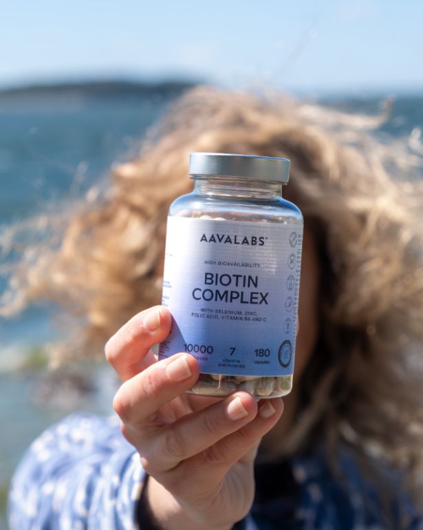 Frau hält Flasche des Biotin Komplex Nahrungsergänzungsmittels vor dem Meer.