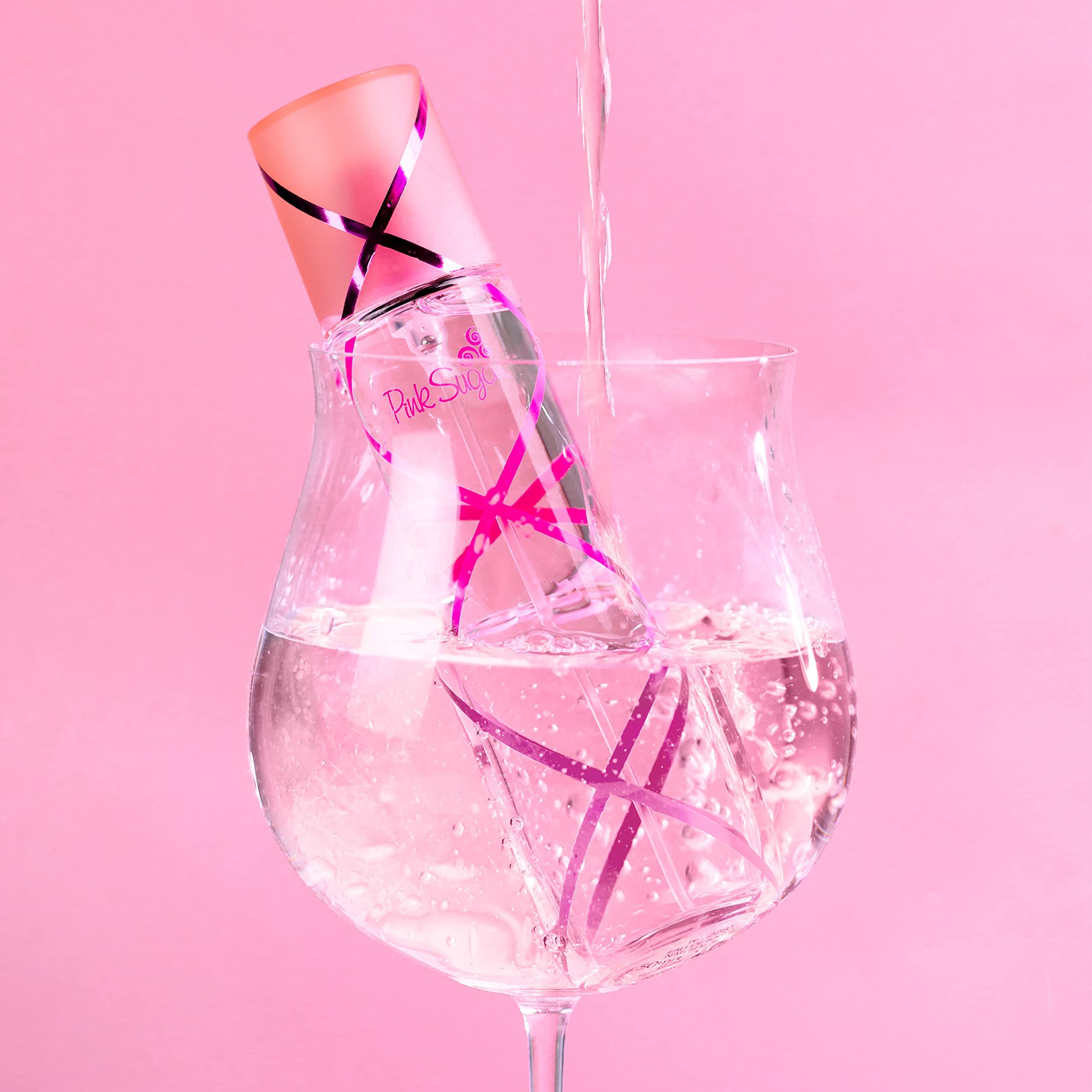 Parfümflasche in einem Glas Wasser. Rosa Hintergrund. Flasche mit rosa Akzenten und Schriftzug.